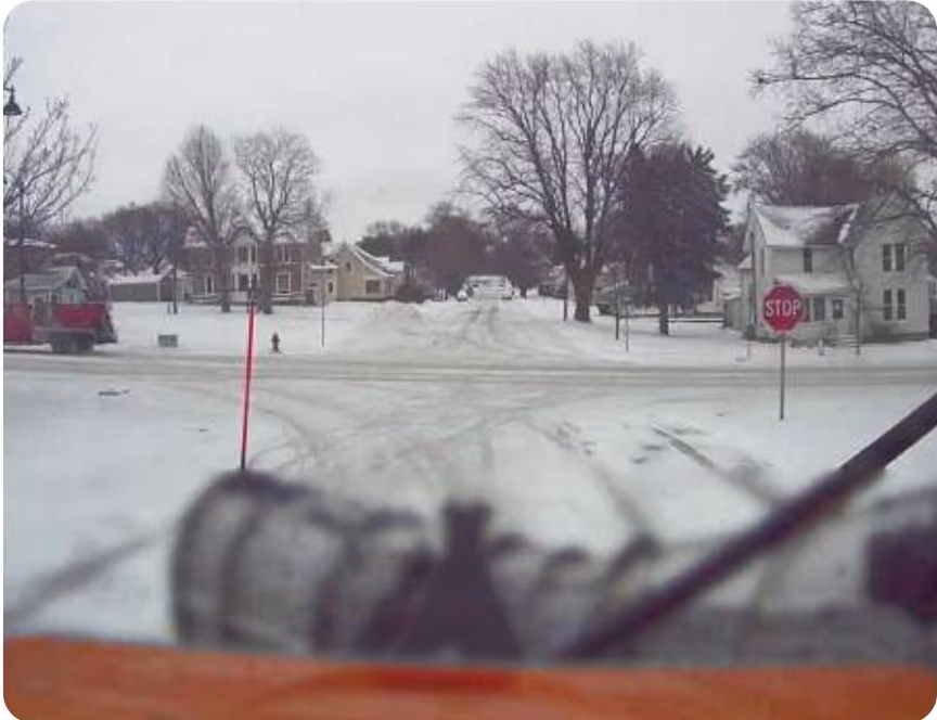 Dash cam view from a snowplow at a snow-covered residential intersection