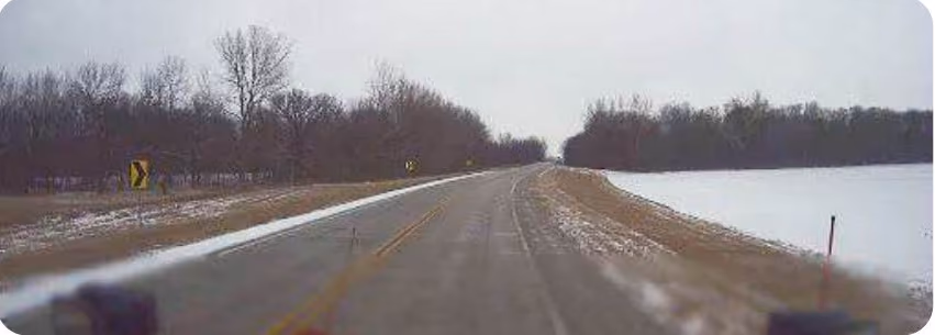 Snowplow dash cam view of a road with patchy snow coverage