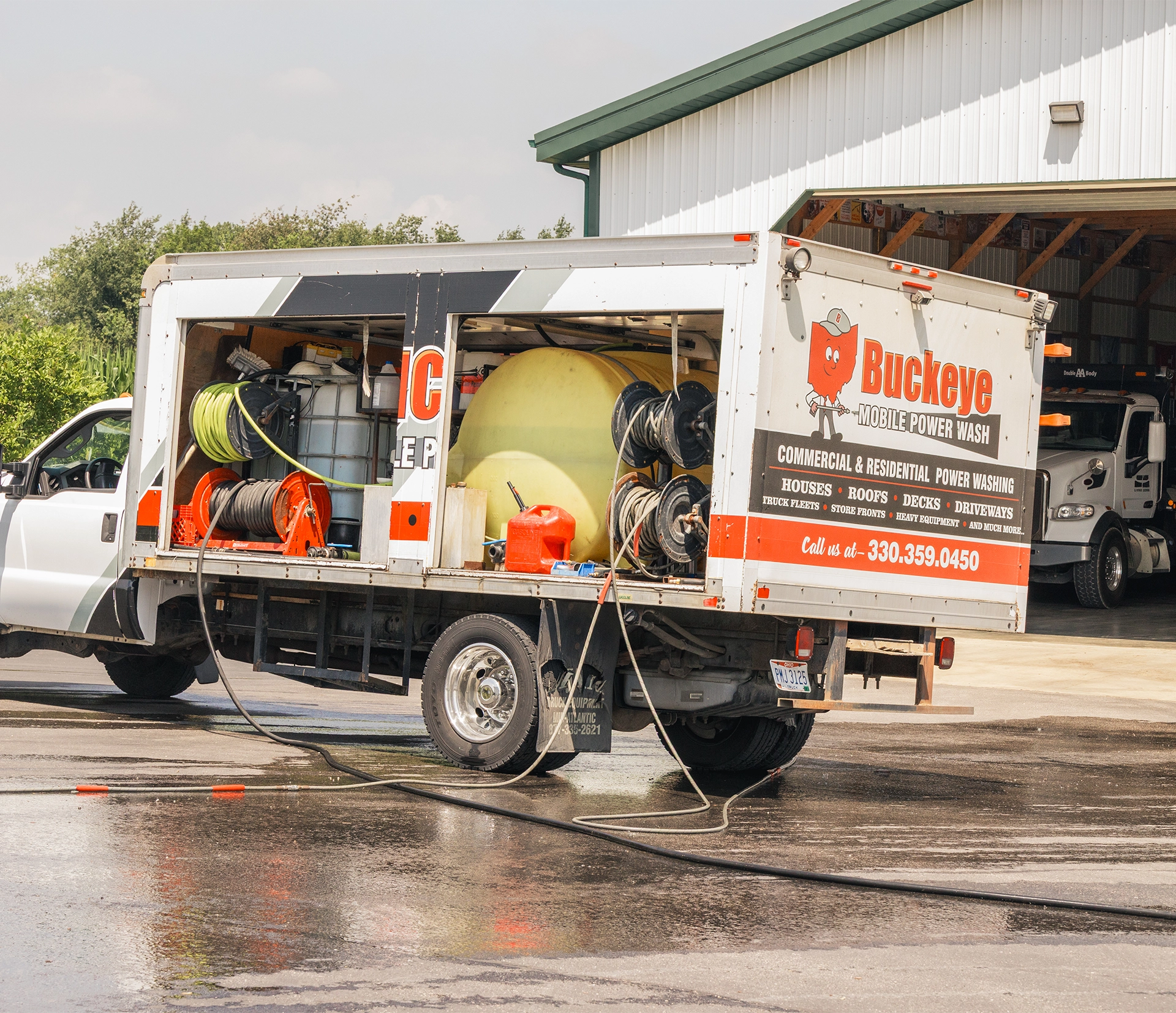 Buckeye Mobile Power Wash truck with hoses and tanks parked near a warehouse on wet pavement.