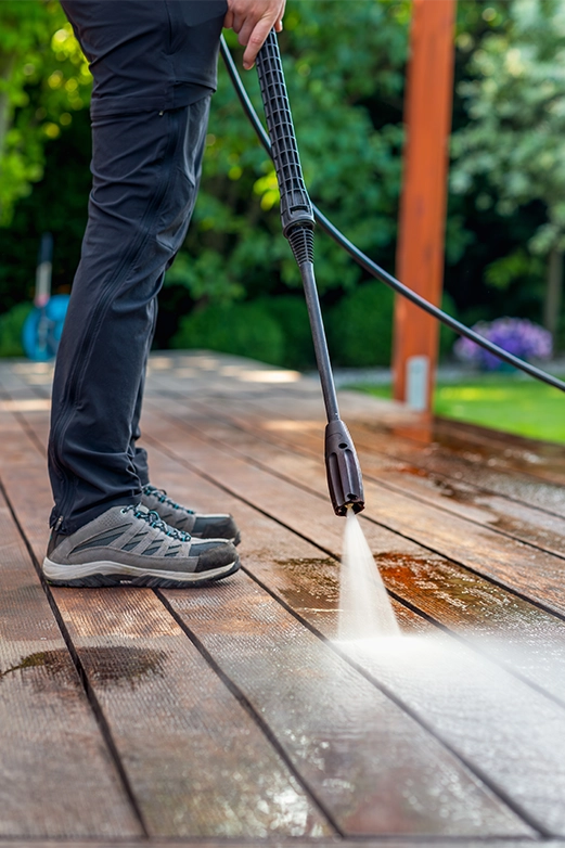 Man on ladder pressure washing a dark shingled roof with a spray nozzle.
