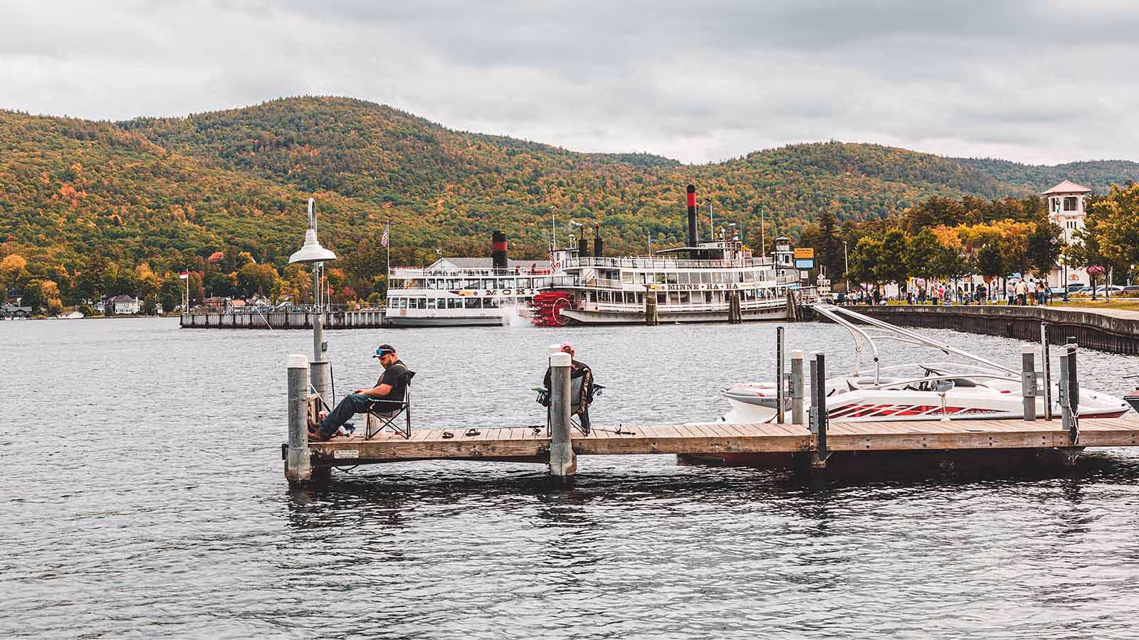 Men fishing off a wooden dock at Lake George, New York, surrounded by calm waters and lush greenery, capturing a peaceful lakeside fishing experience in the Adirondacks.