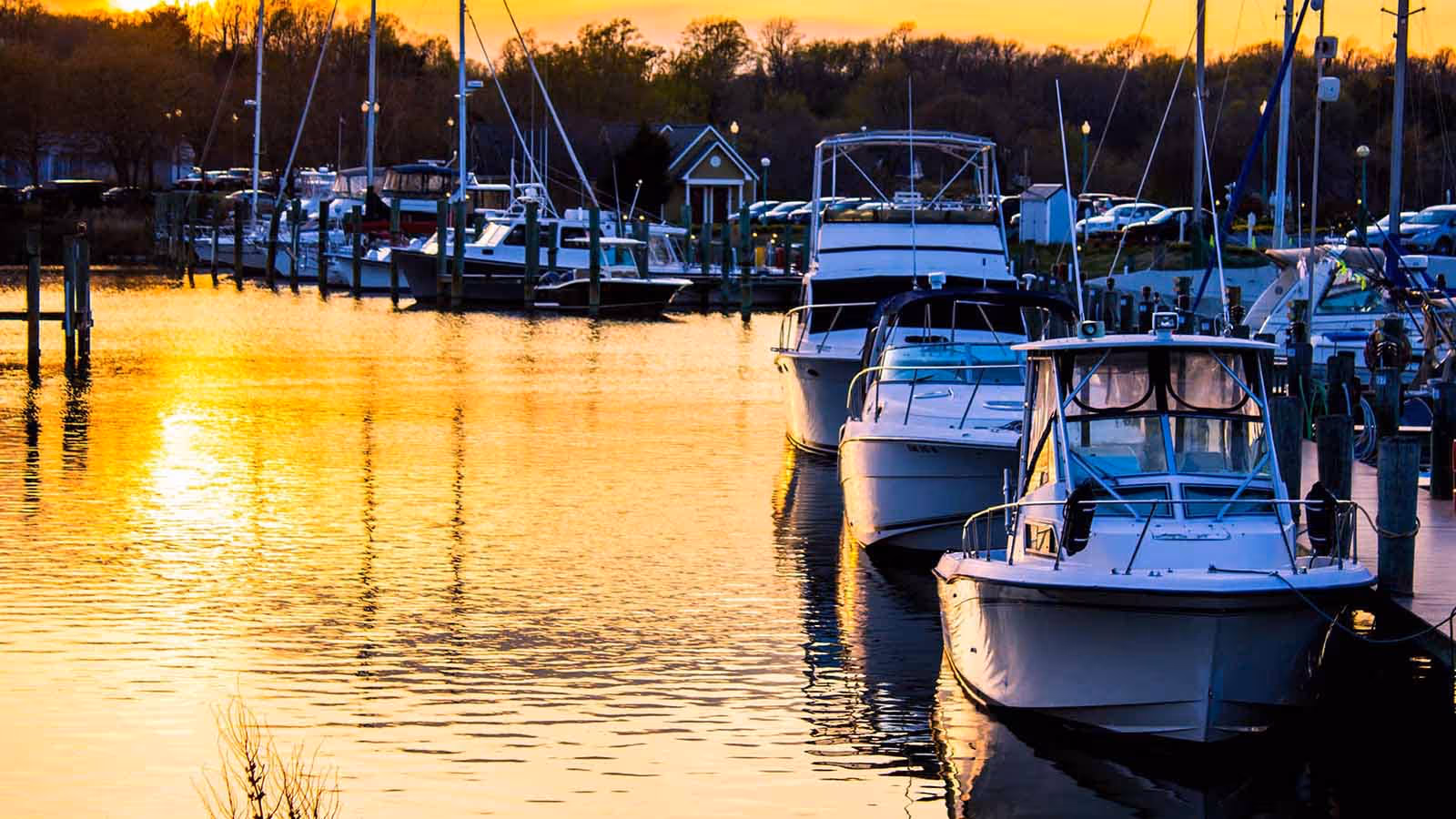 Boats anchored in Chesapeake Bay at sunset with vibrant orange and pink skies reflecting on the calm water, capturing the serene coastal boating lifestyle and natural beauty of the Chesapeake region.