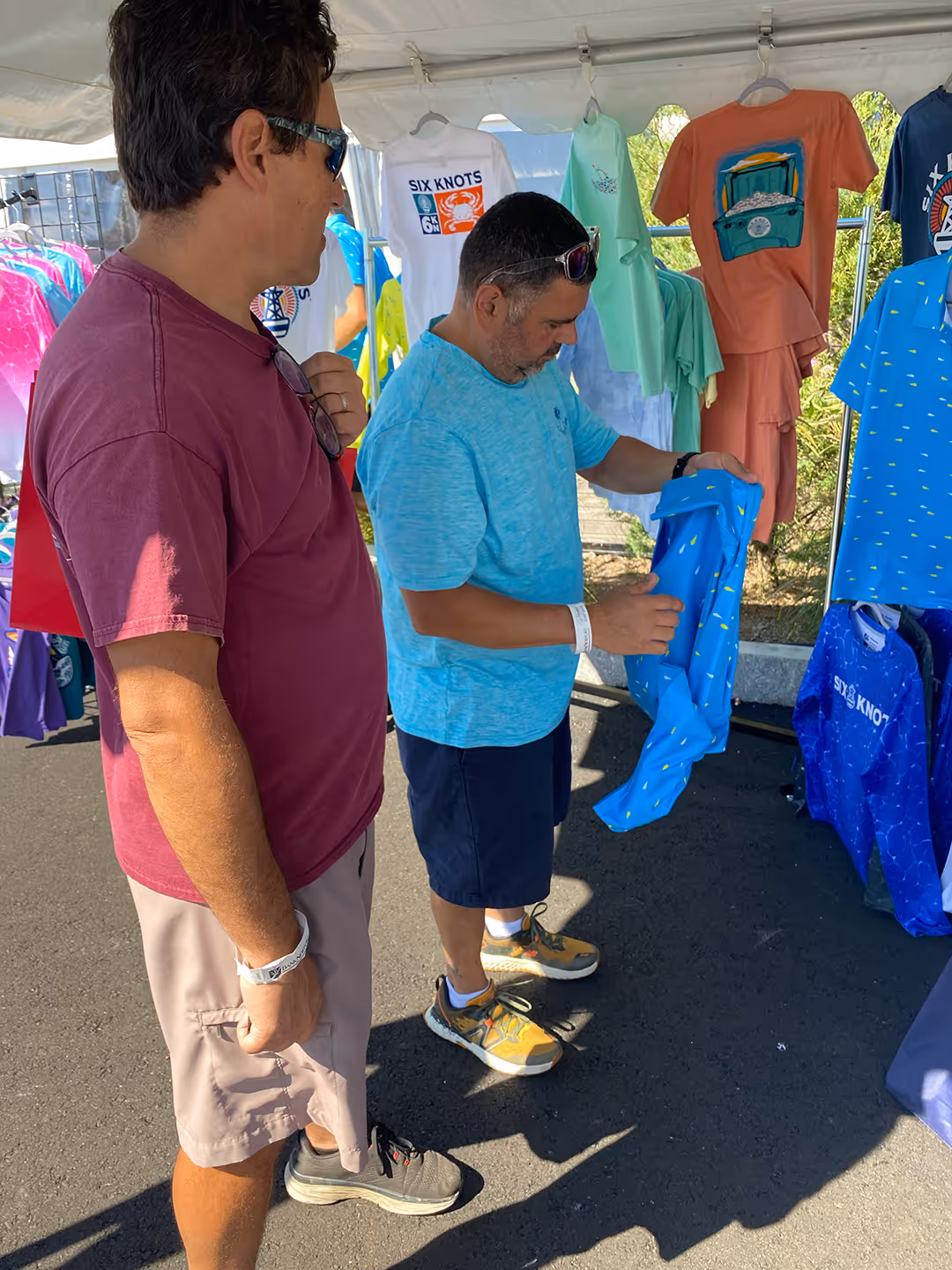 Shoppers exploring the Six Knots booth, looking closely at a Mahi Mahi Performance Polo Shirt