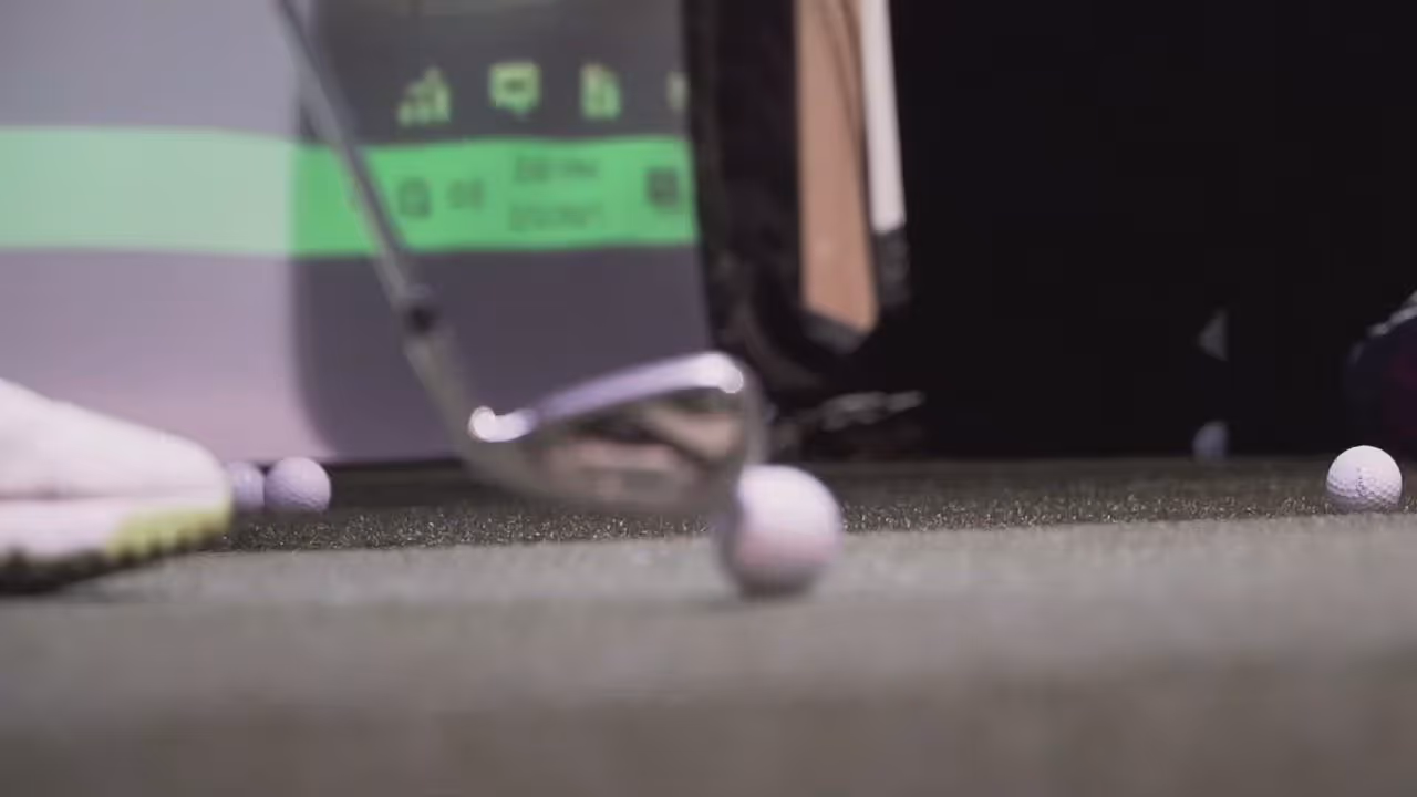 Close-up of a golf club hitting a golf ball on artificial turf with other balls nearby.