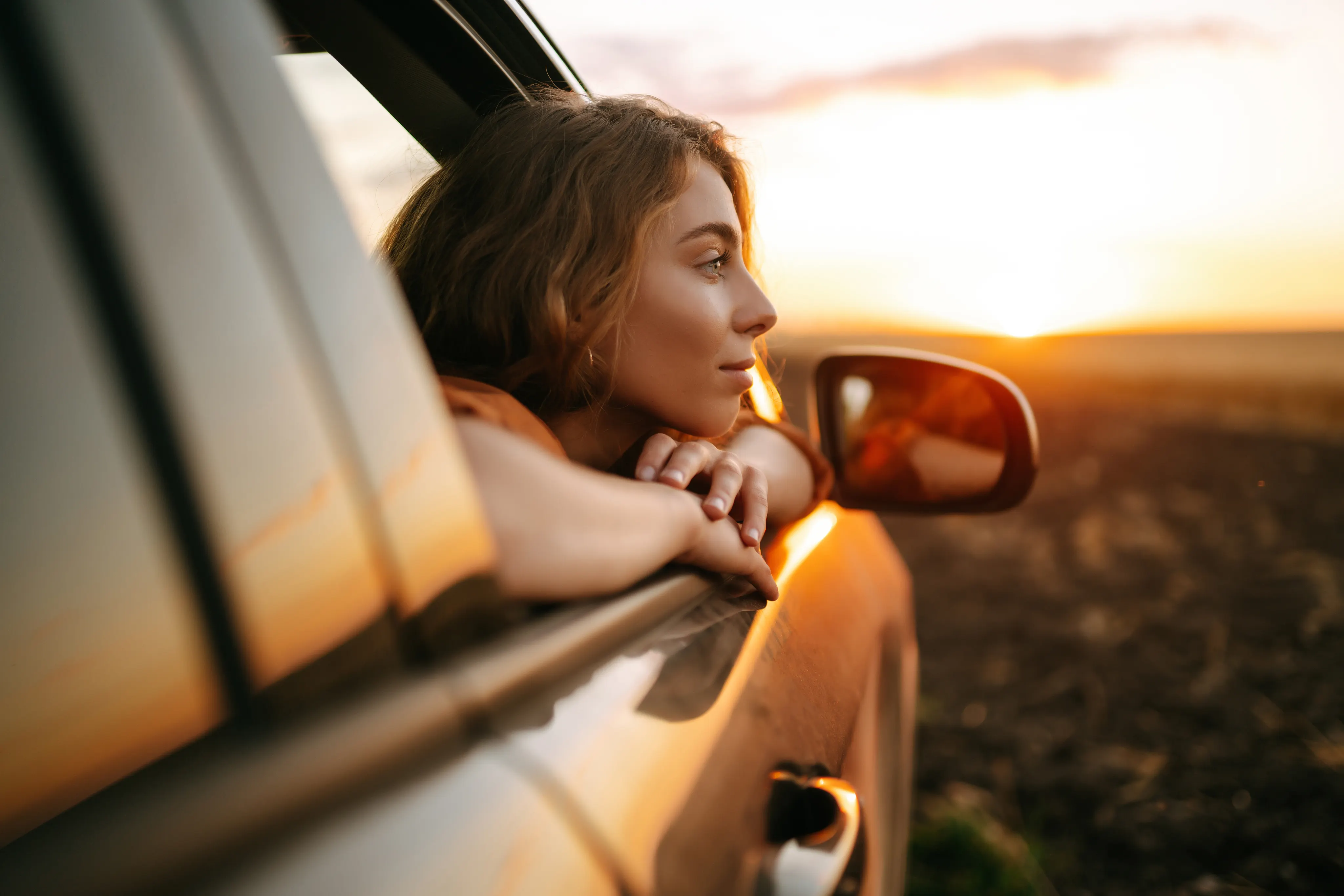 A woman looking out the window of a parked car at sunset.
