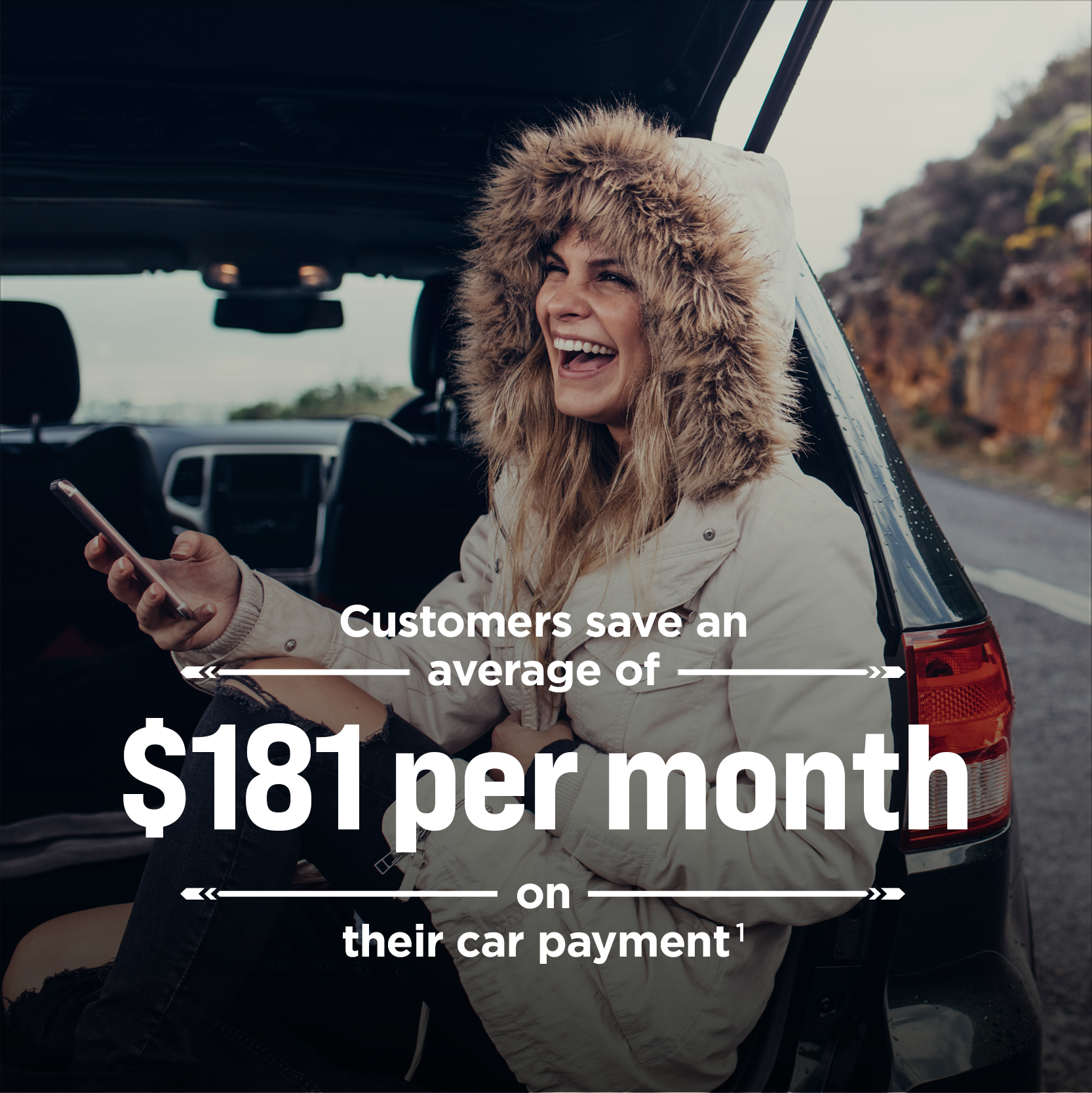 Image of a woman holding a mobile phone and laughing while seated in the open rear hatch of a vehicle