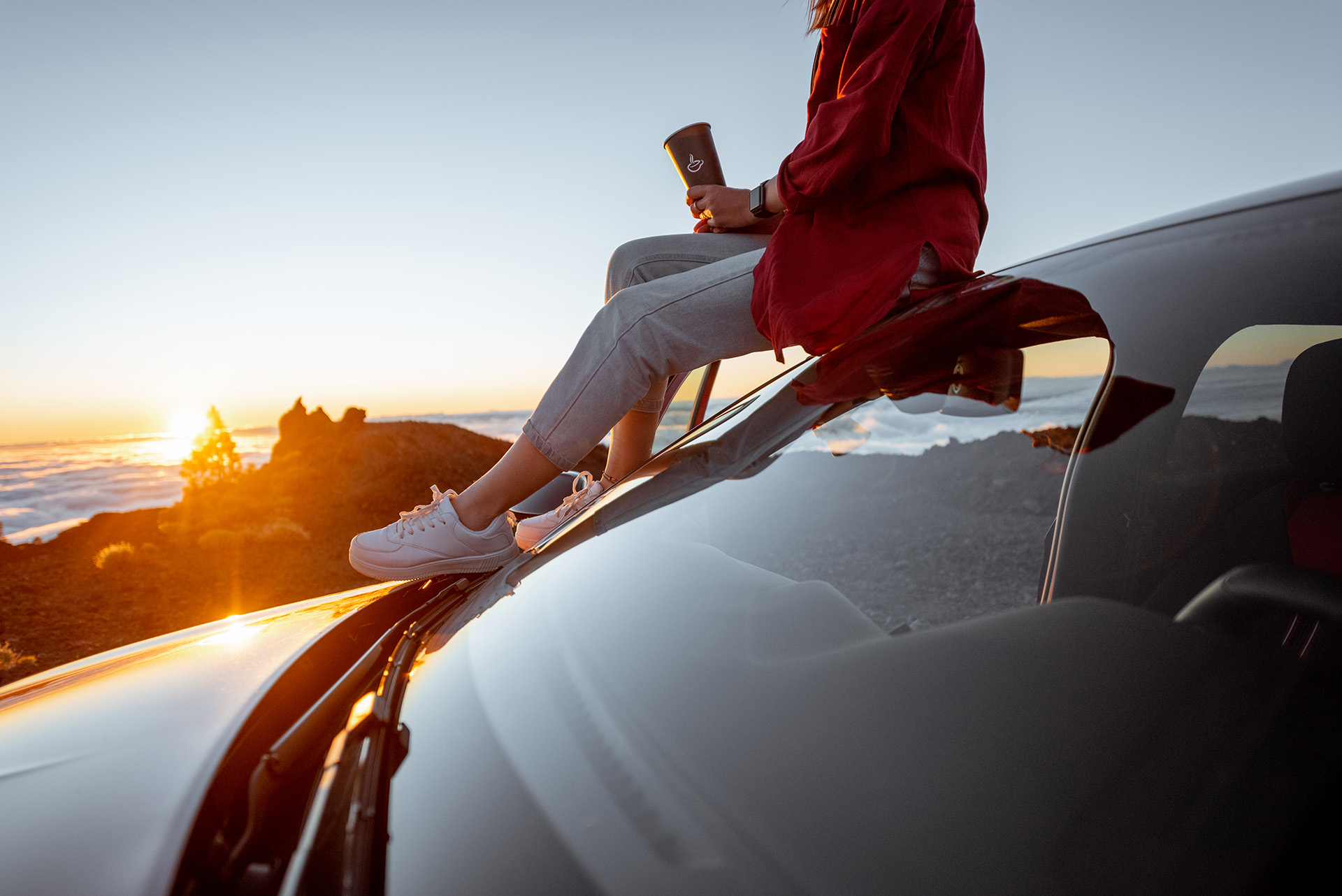 Image of a woman watching the sunset while seated on the roof of a parked vehicle