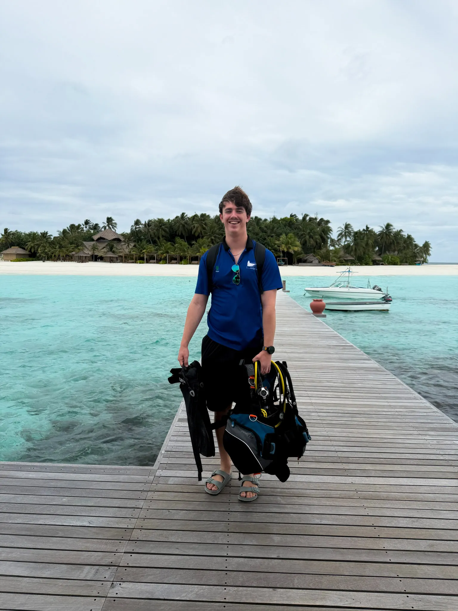 Man med snorkelutrustning står på en brygga över turkost vatten, med en grön ö i bakgrunden