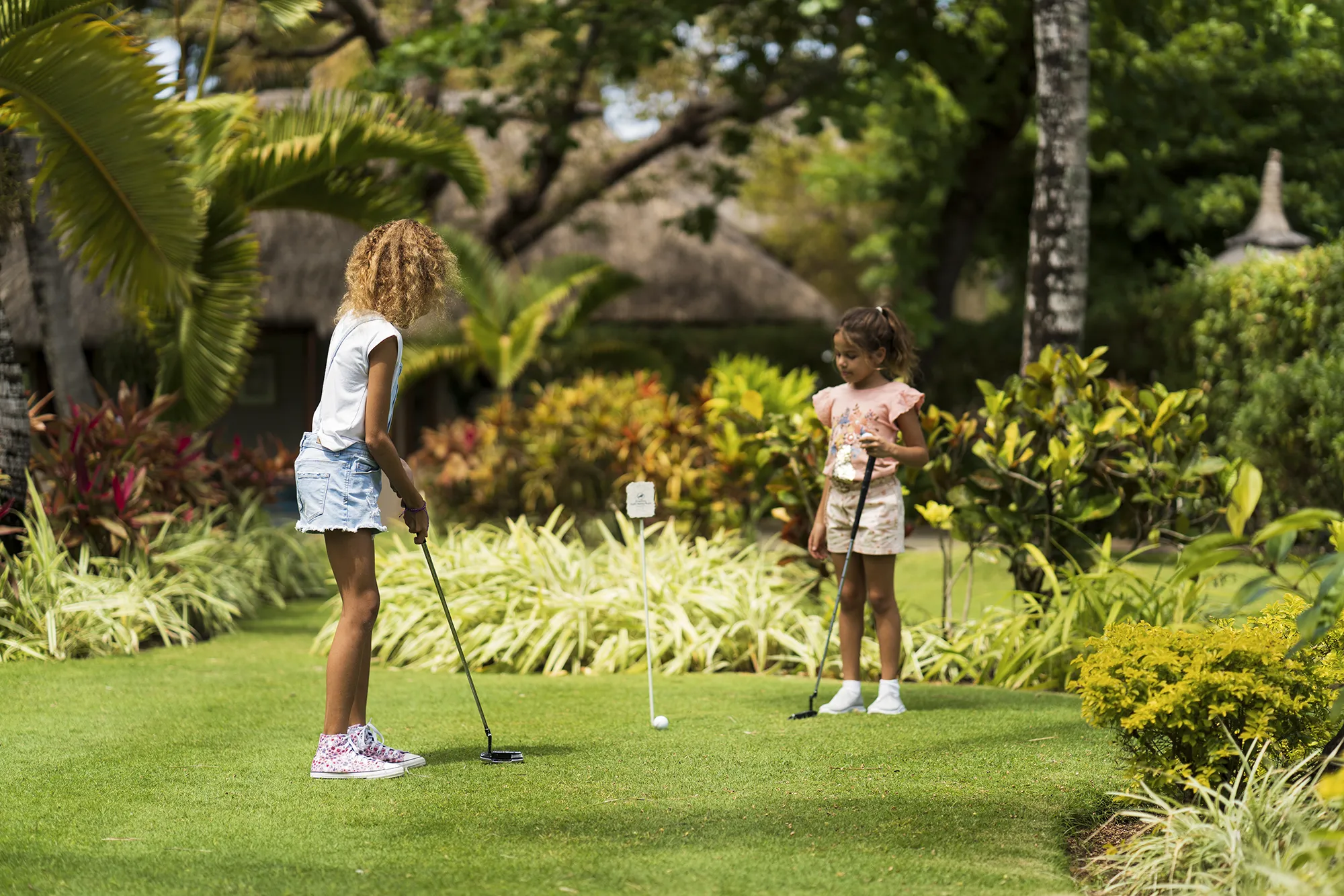 Två barn spelar minigolf på en gräsmatta omgiven av tropiska växter
