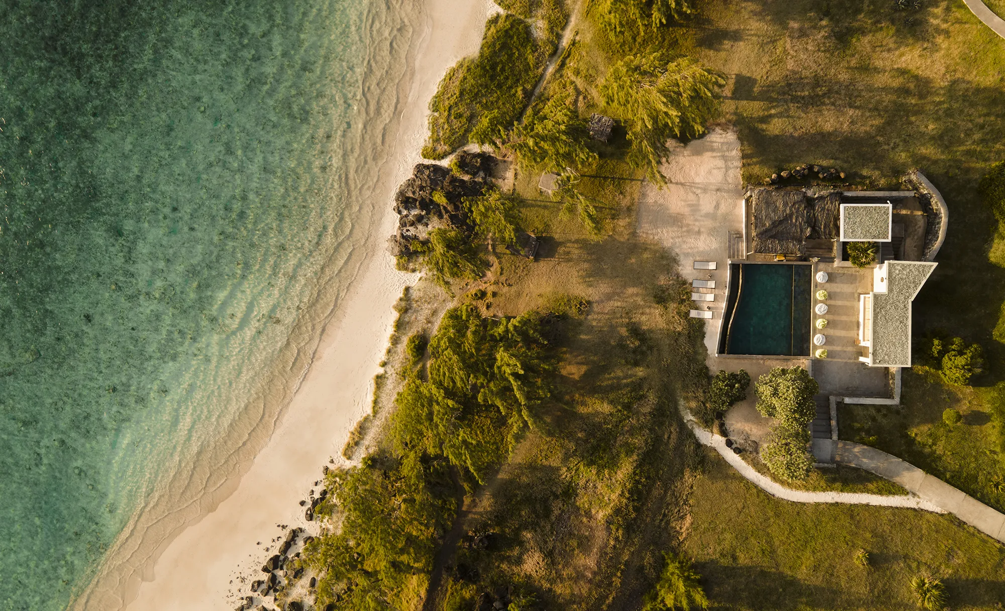 Flygbild över en villa med privat pool intill en ljus sandstrand och turkost vatten