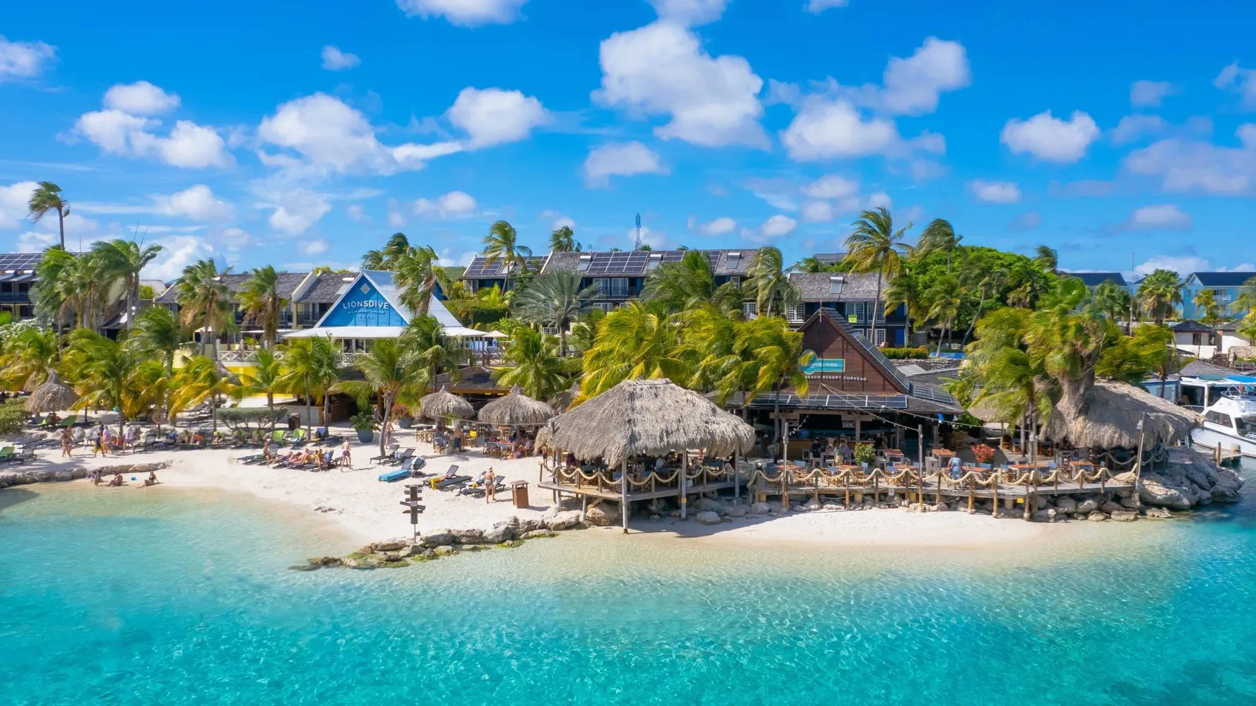     Flygvy över strandresort på Curaçao med palmer, vita sandstränder och kristallklart karibiskt vatten.