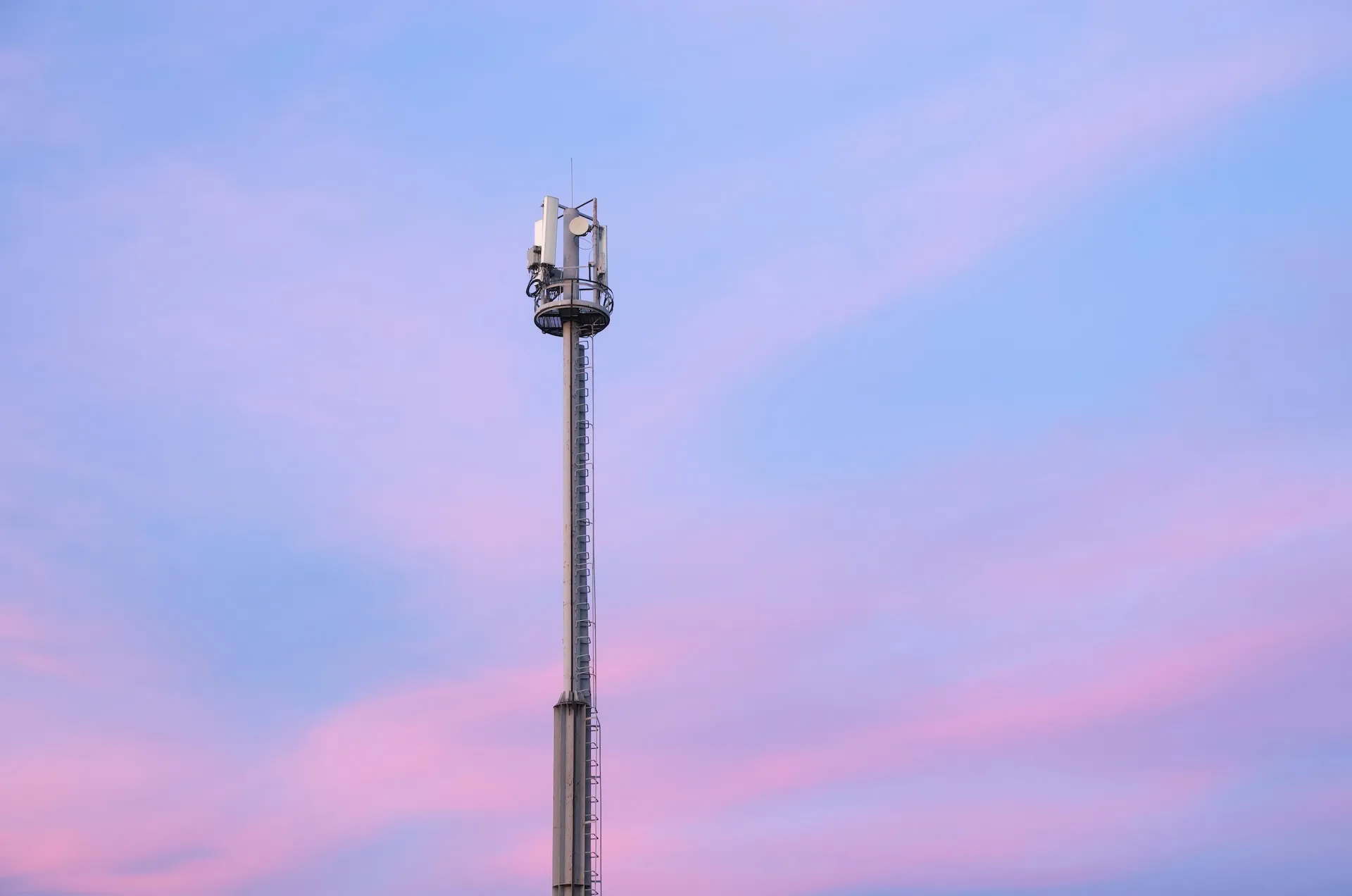 Tall cell phone tower against a pastel pink and blue sky at sunset.