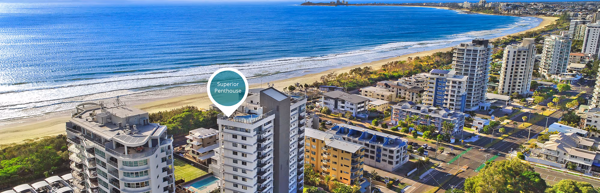 Aerial view of a coastal city with high-rise buildings along a sandy beach and a marker indicating a superior penthouse.