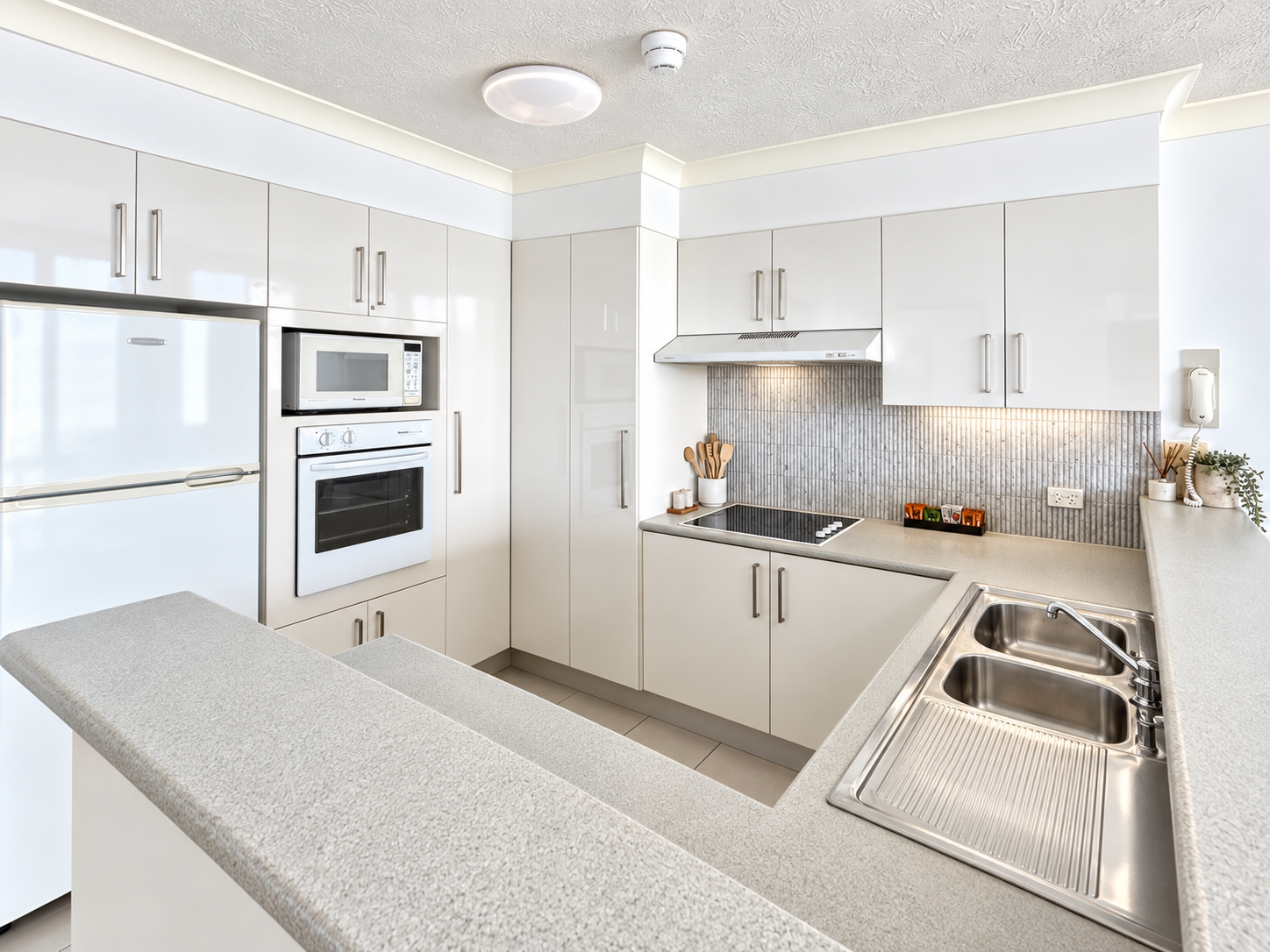 Modern kitchen with white cabinets, a white refrigerator, built-in microwave and oven, electric stove with hood, double stainless steel sink, and light gray countertops.