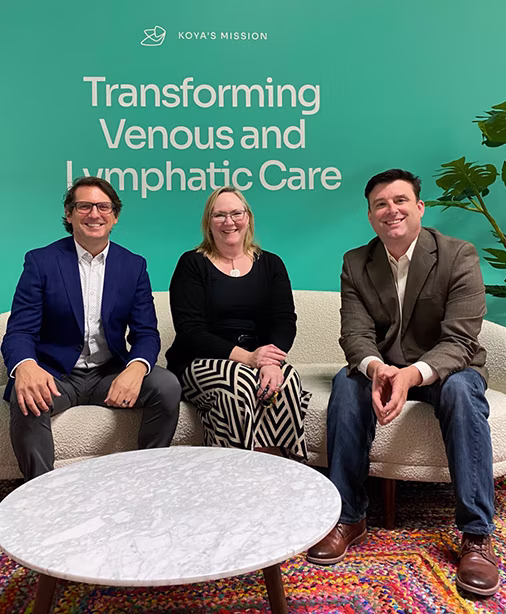 Three Koya Medical employees in front of a sign that says Koya's Mission, Transforming Venous and Lymphatic Care