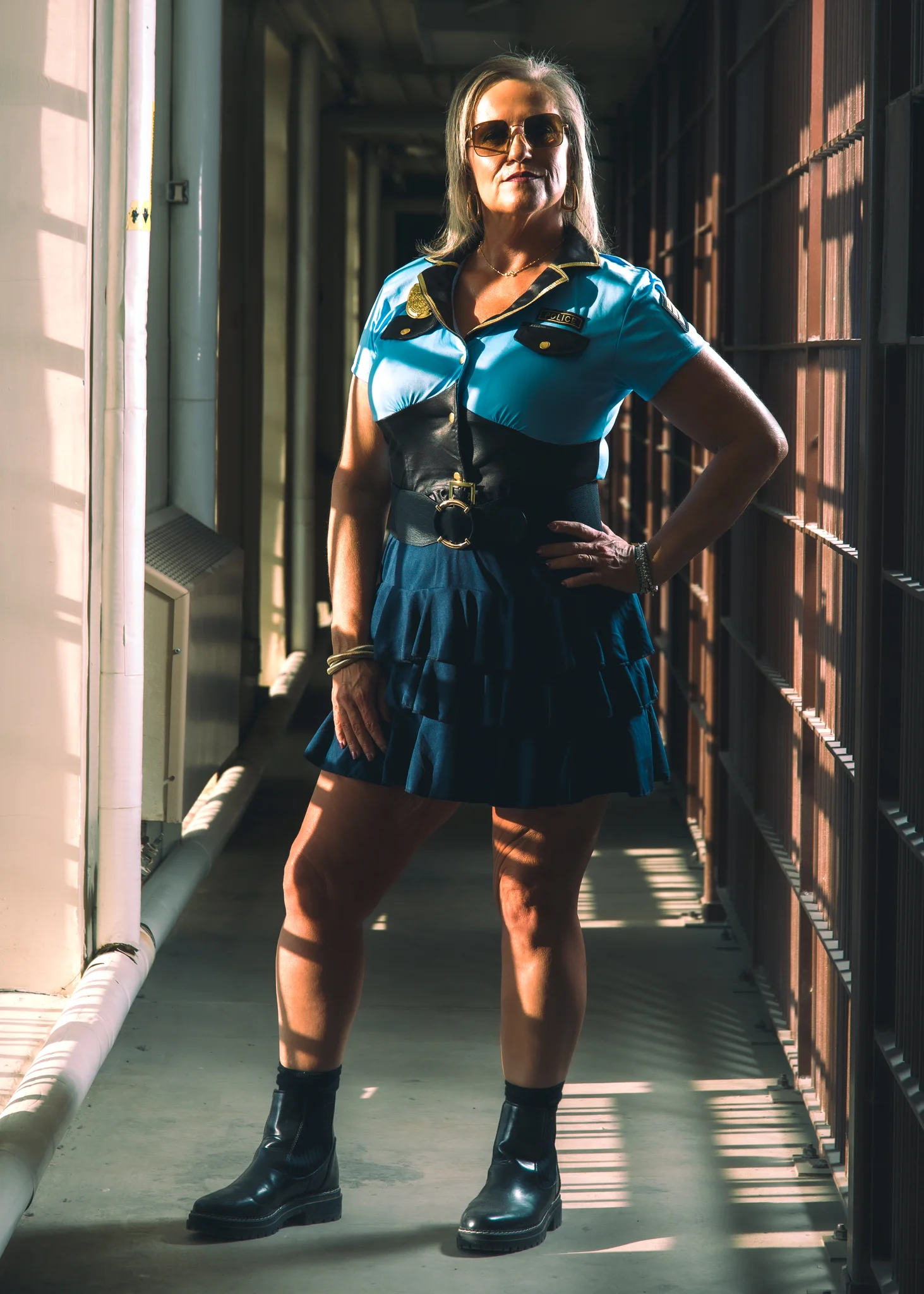A Dark Prison performer in a blue police costume stands in a sunlit prison corridor.