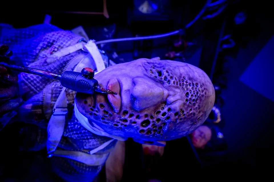 A textured creature prop lies beneath a metal instrument in intense blue light.