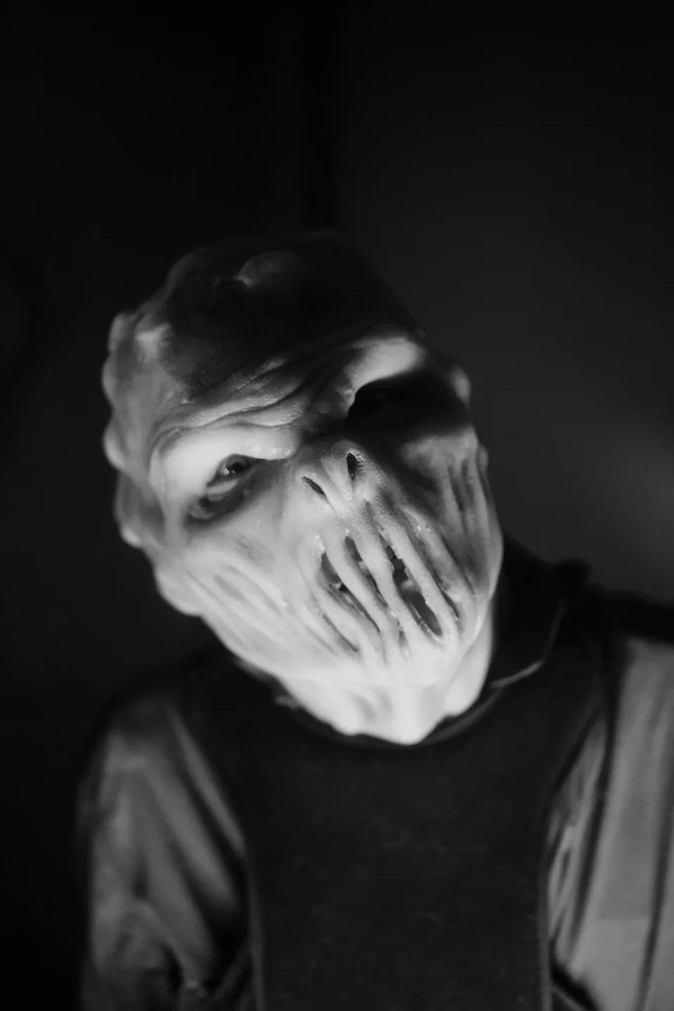 A mouthless creature tilts its head in the darkness.