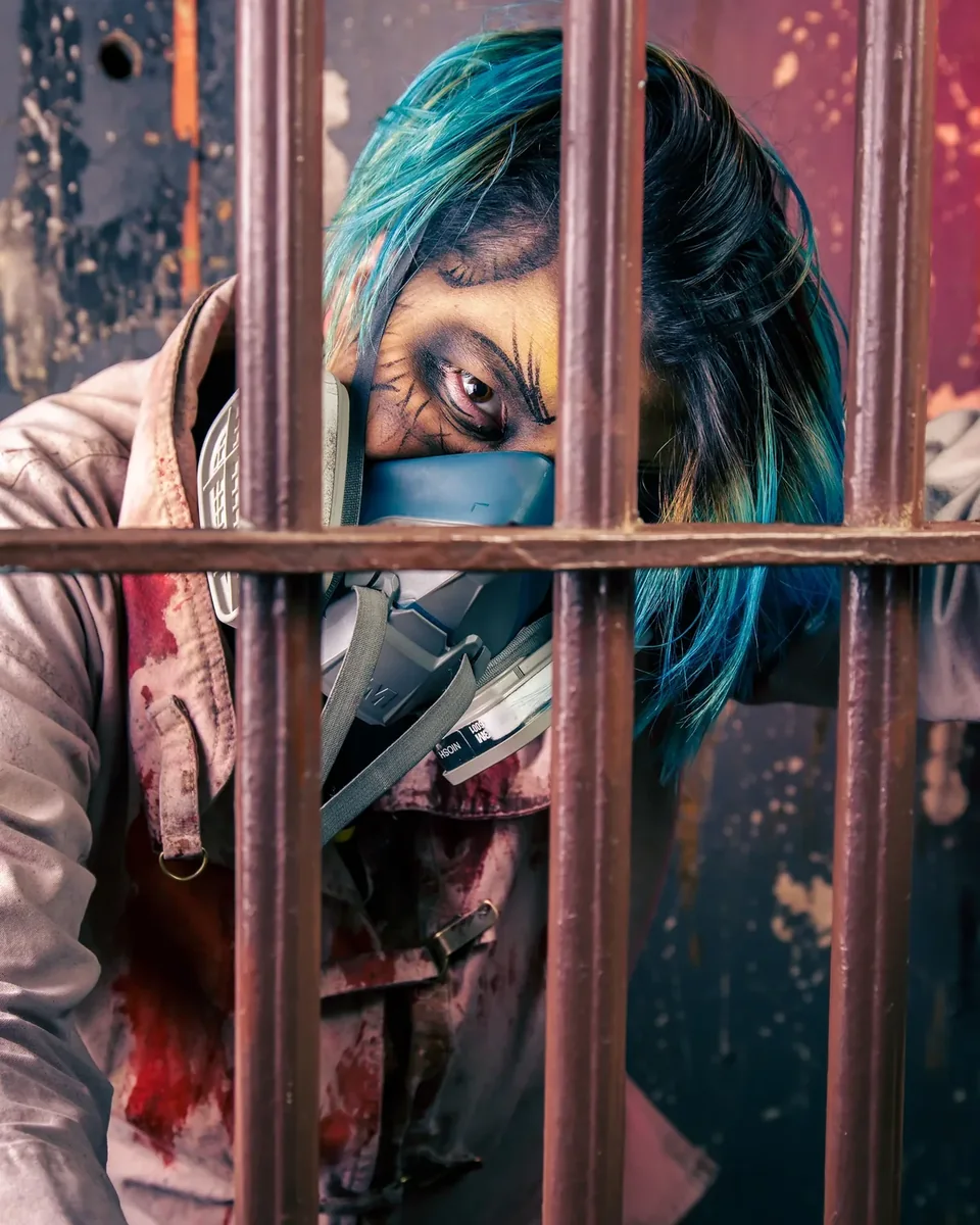 A blue-haired character peering through rusted prison bars.