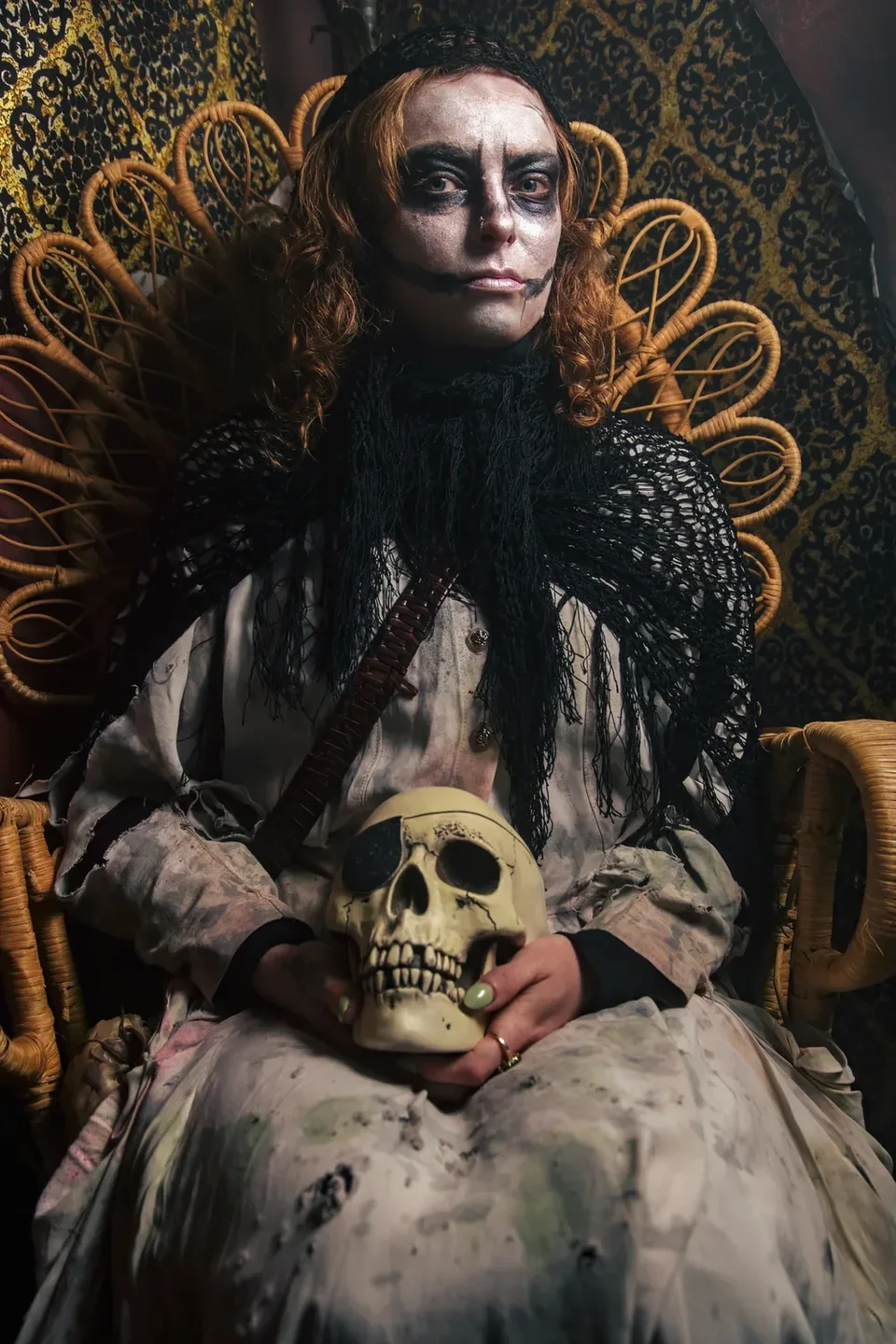 A witch seated in an ornate chair holding a skull.