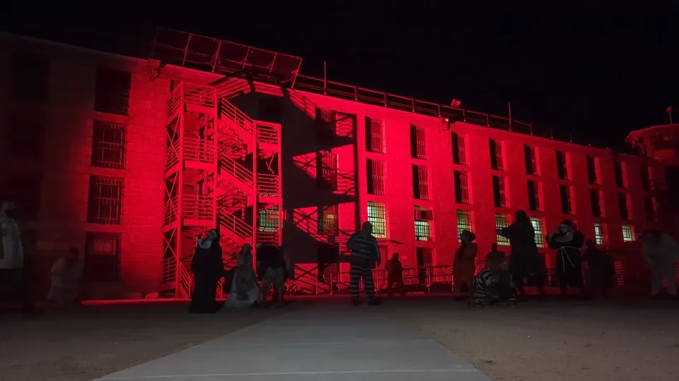 The prison facade illuminated in red at night, with a gathering in the yard.