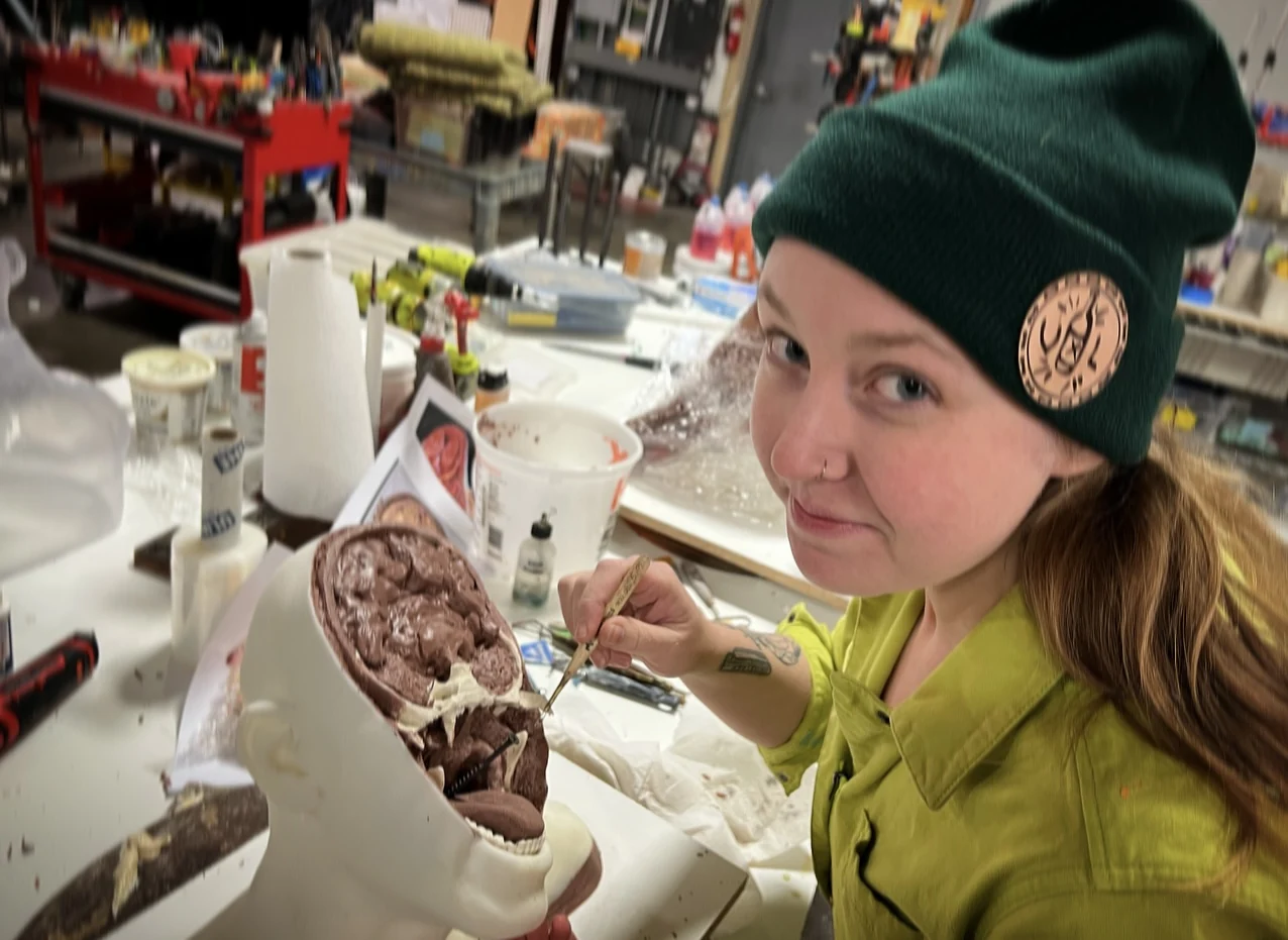 An artist painting a creature head at a workshop table