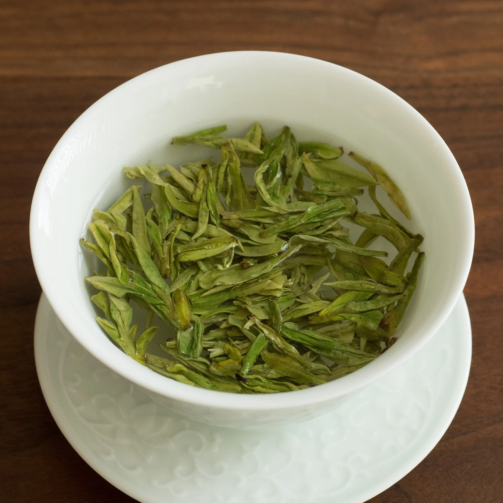 Green tea leaves steeping in a white lidded gaiwan