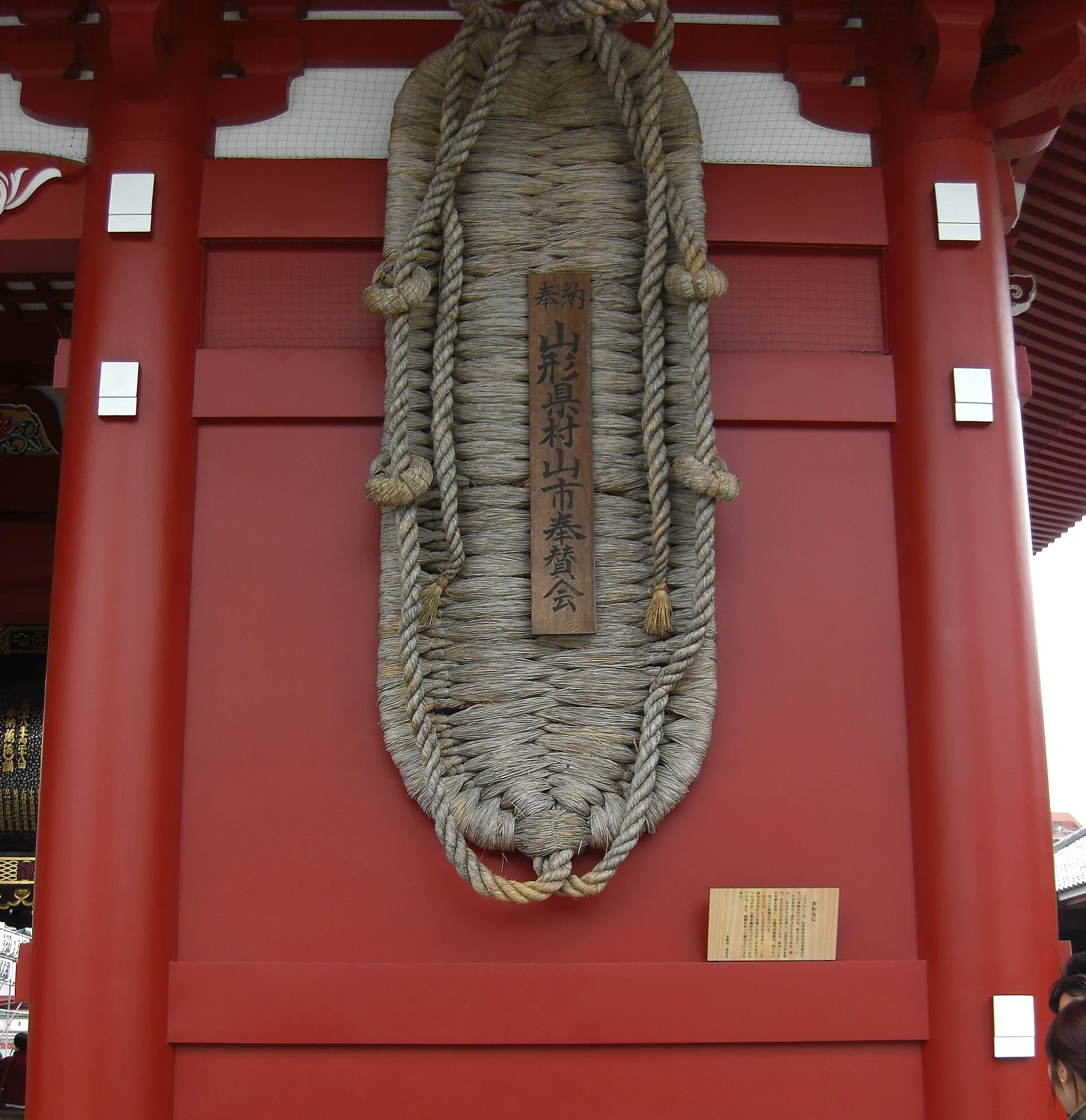Huge woven straw sandal hanging on the side of a red temple gate