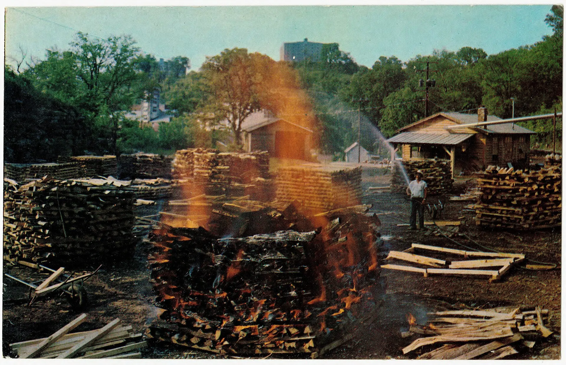 Postcard of a large stack of burning wood for charcoal at the Jack Daniel Distillery