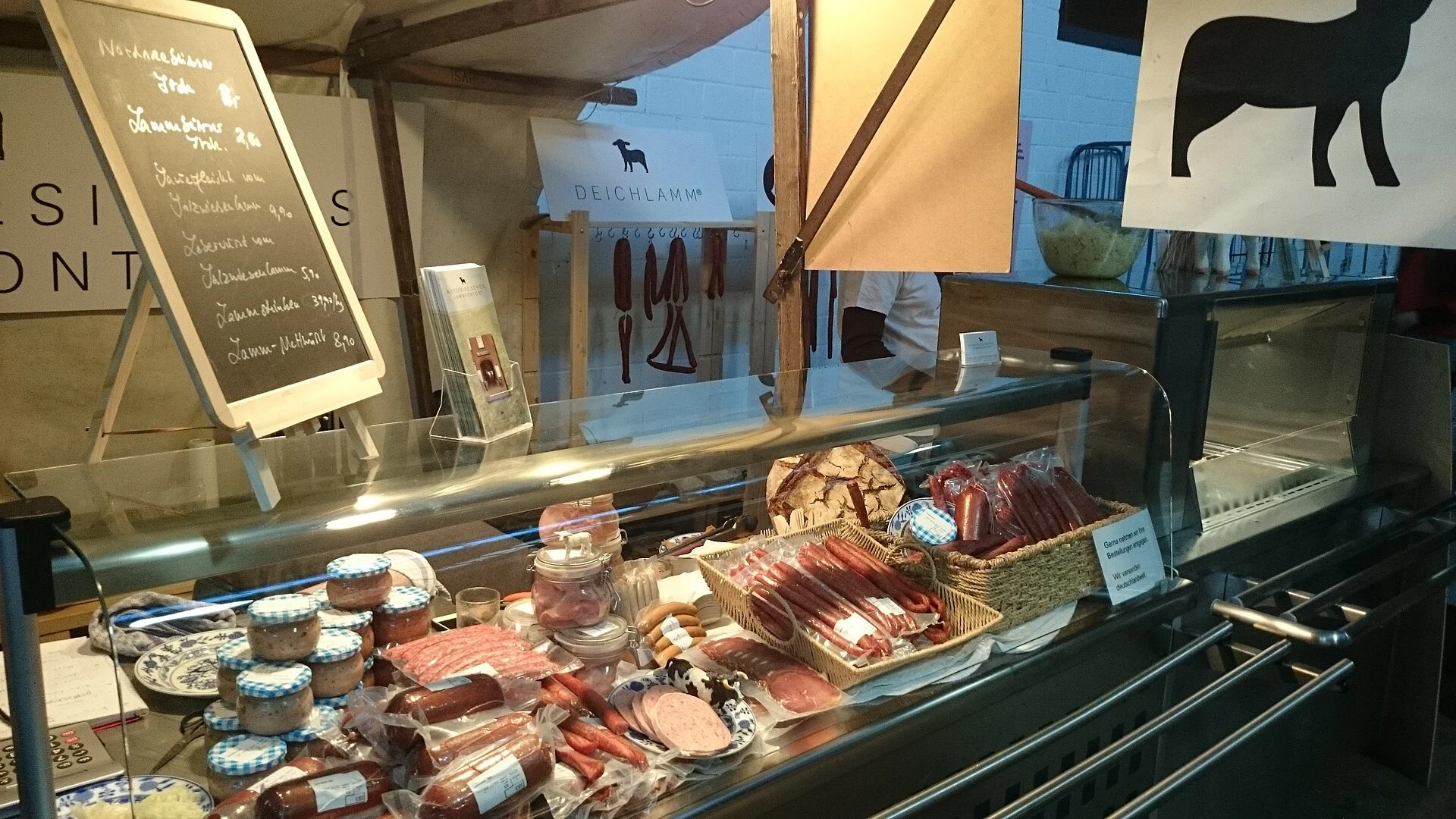 Glass deli counter with cured meats and chalkboard menus in a Berlin market hall