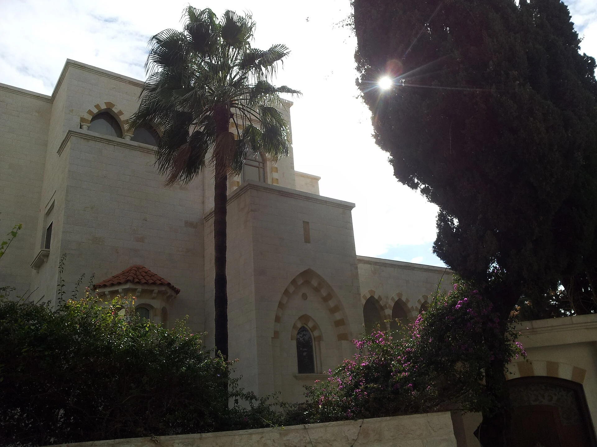 Pale limestone house with arched windows beside a palm tree