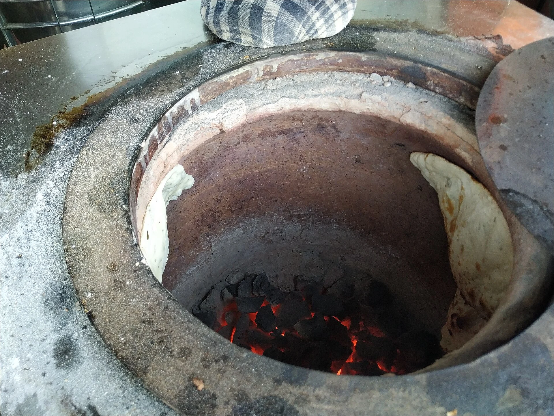 Naan stuck to the inner wall of a tandoor above glowing charcoal