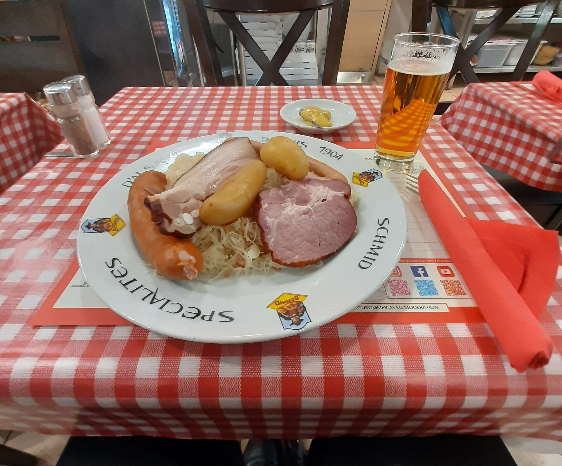 Plate of choucroute garnie with sausages and ham beside a glass of beer