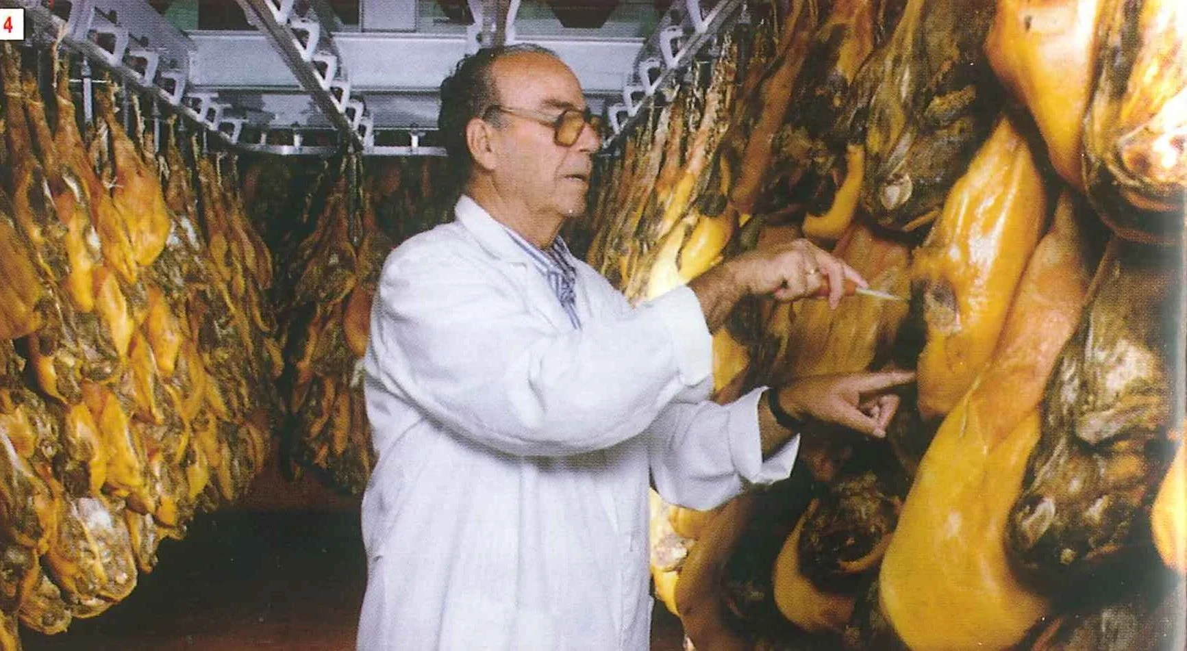 Man in a white coat testing hanging hams in a drying room