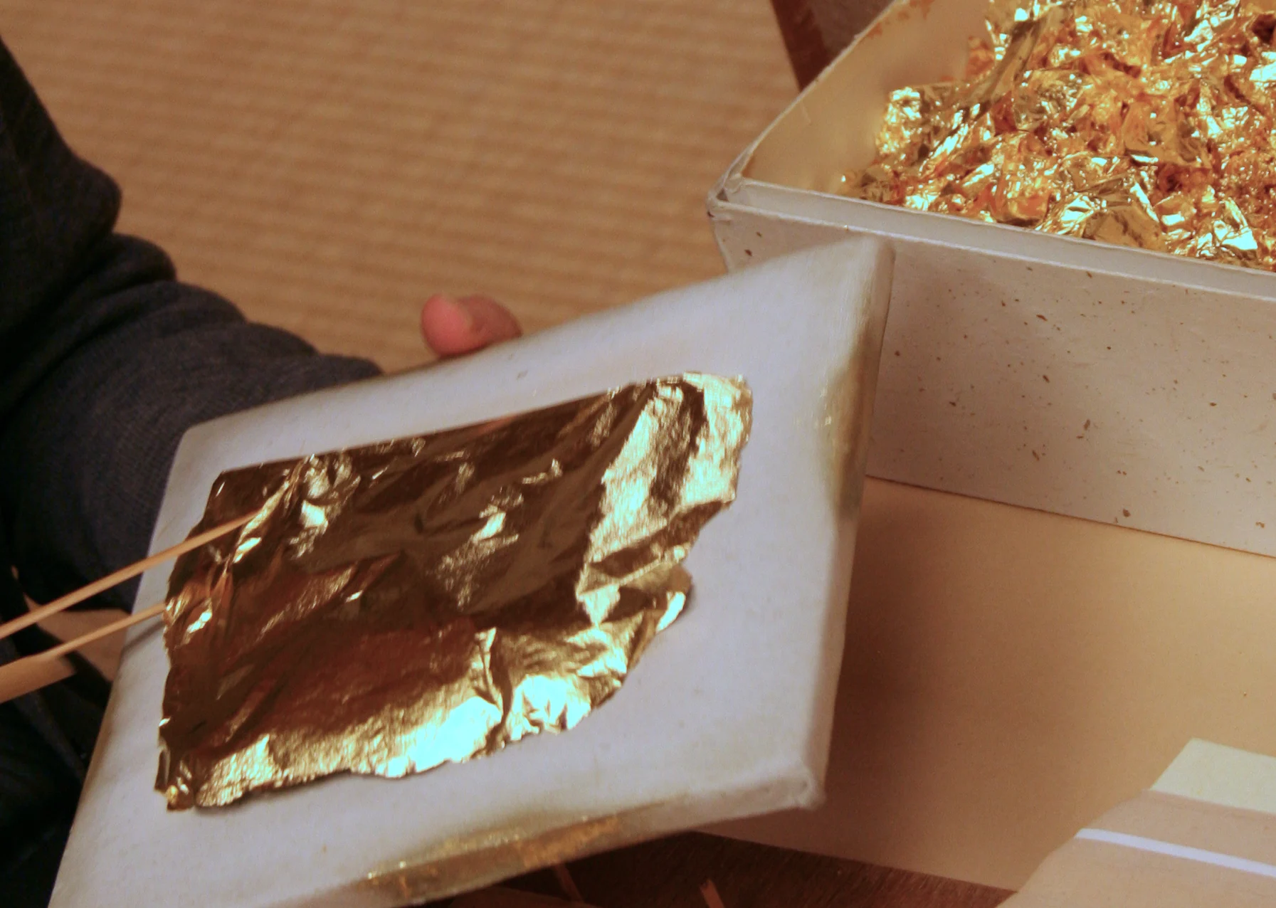 Gold leaf sheet being lifted with bamboo tweezers in a Kanazawa workshop