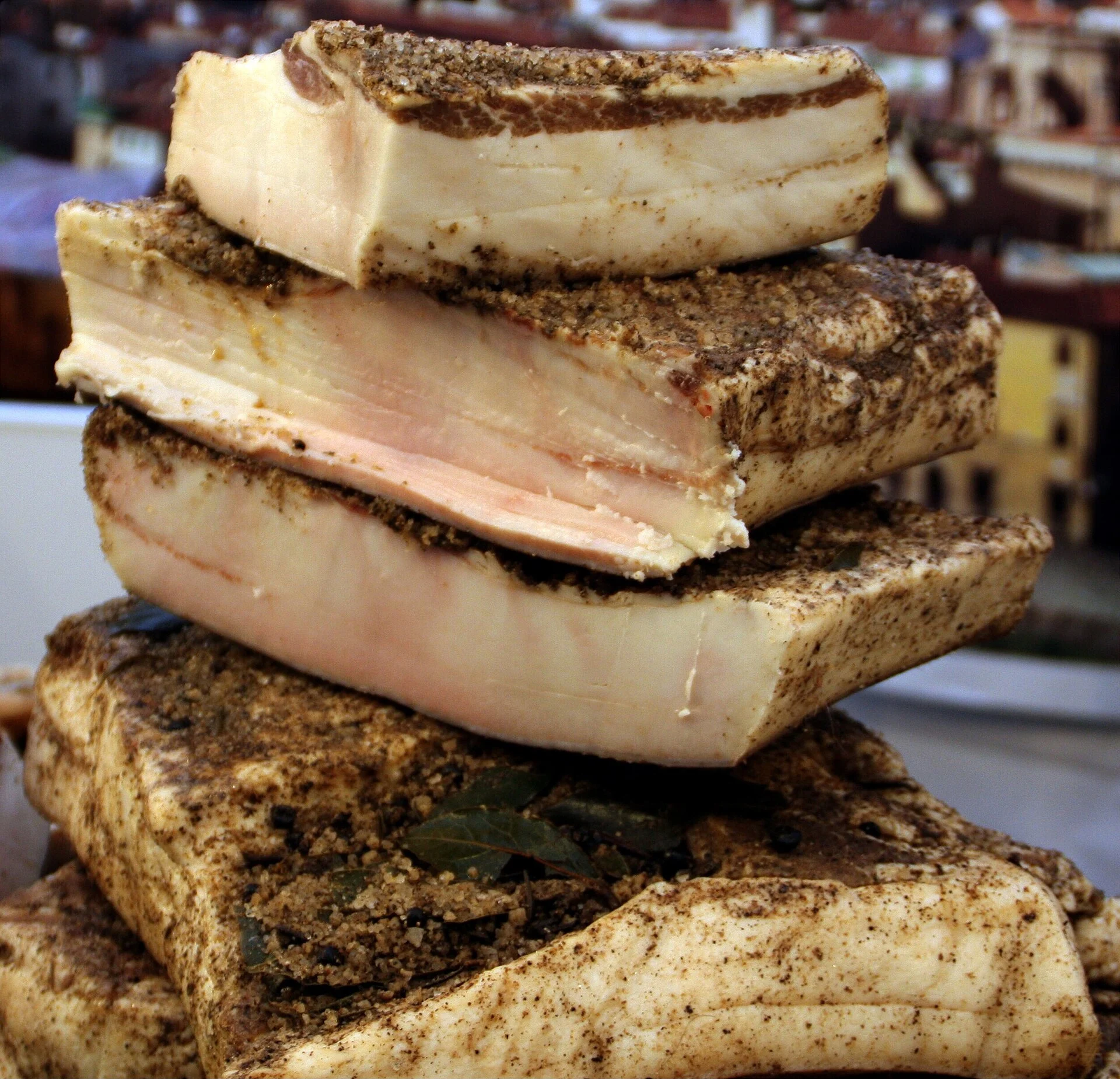 Stacked slabs of white cured pork fat coated in herbs and salt