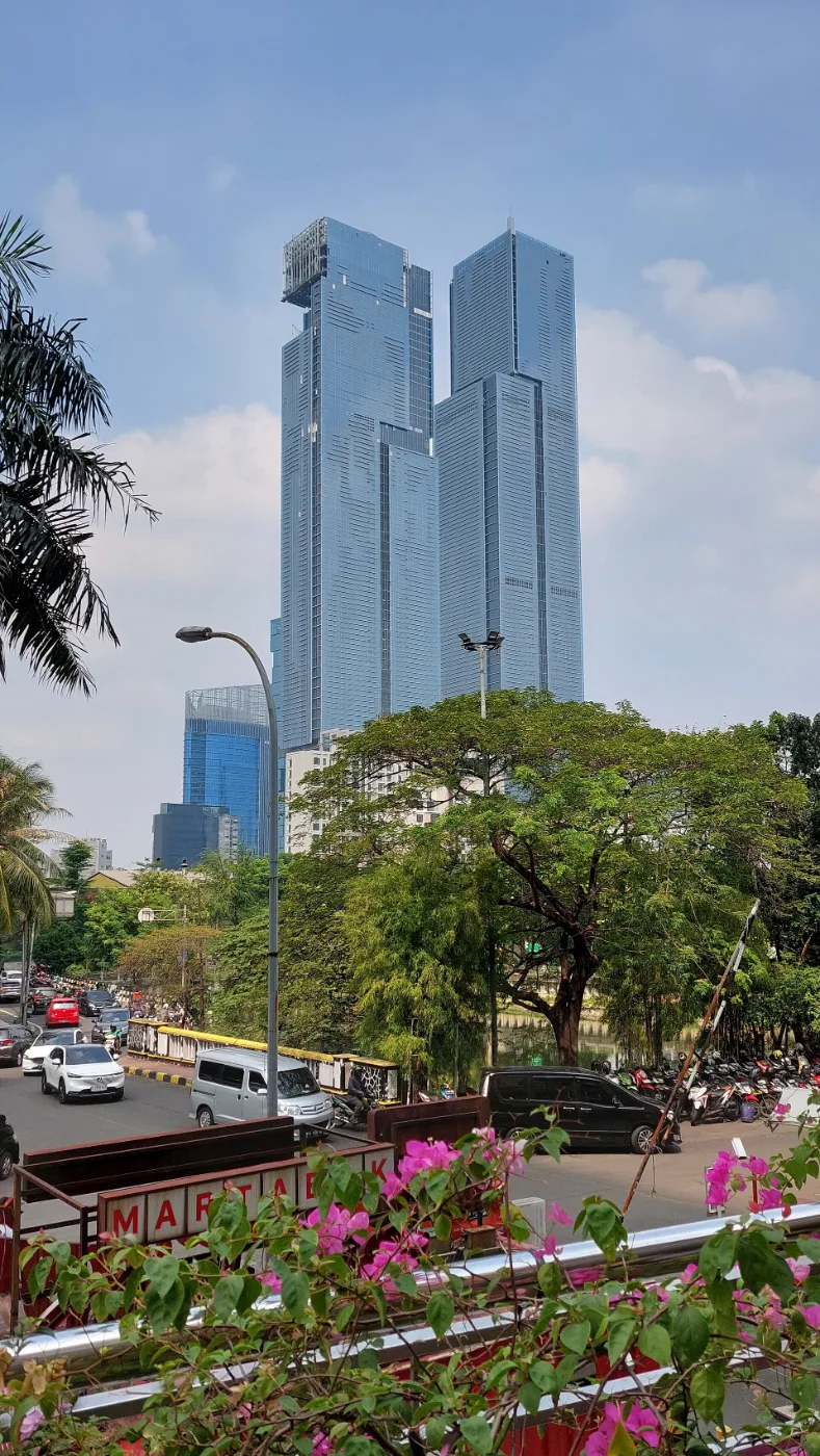 Two tall blue glass towers rising above trees and a street