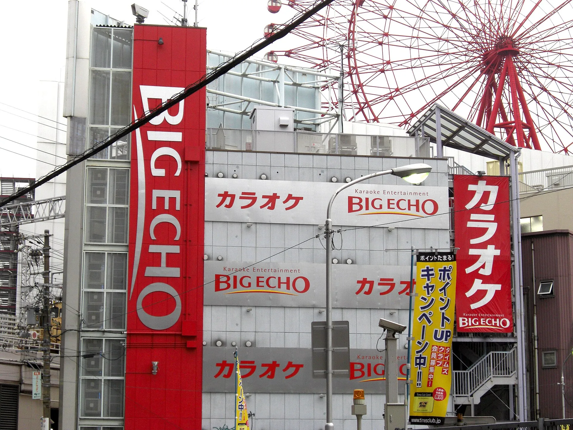 Multi-storey building with red Big Echo karaoke signs beside a Ferris wheel
