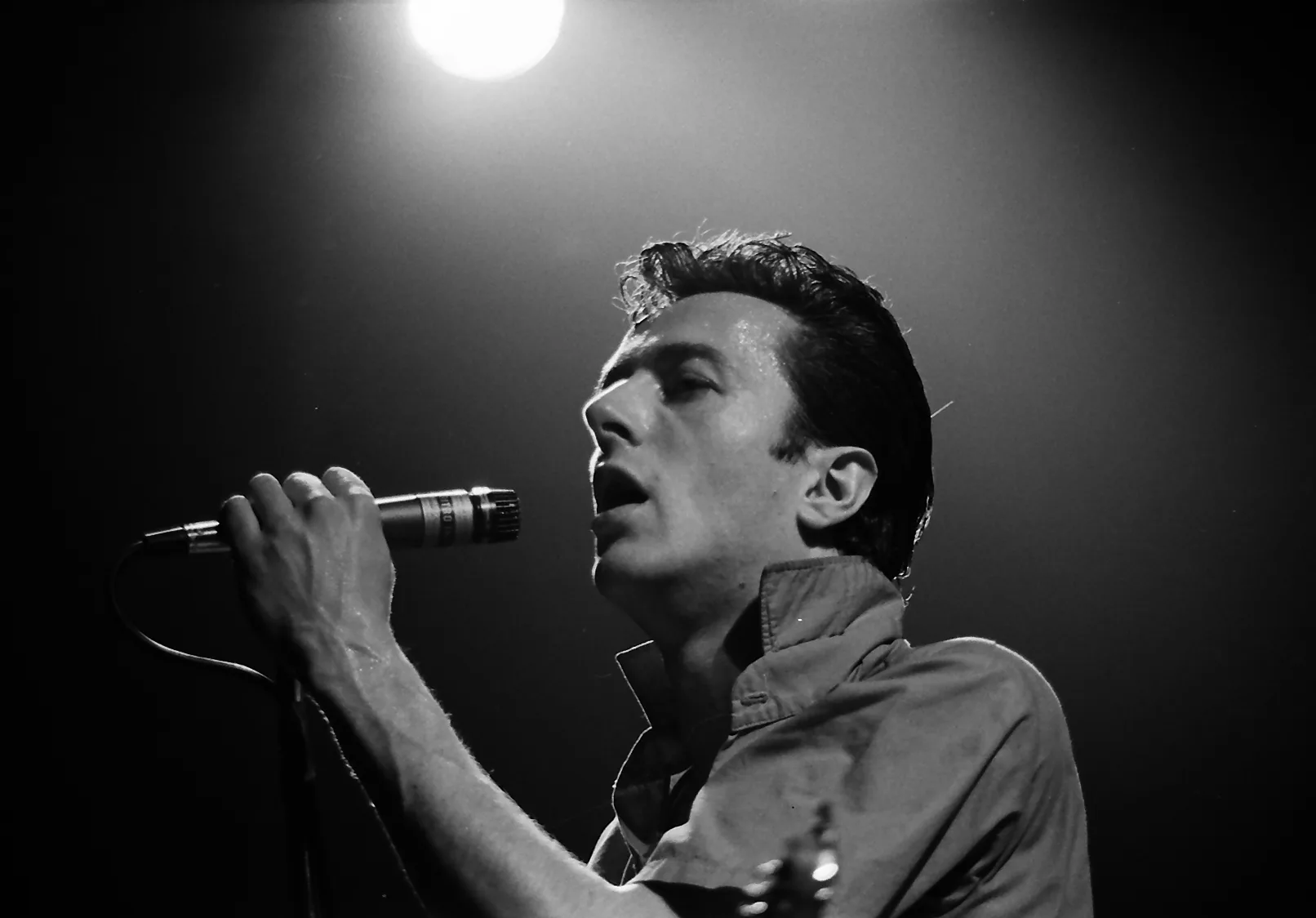 Black and white photograph of Joe Strummer singing into a microphone