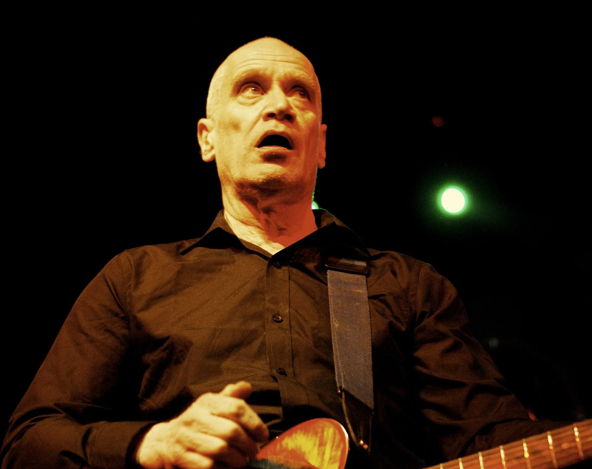 Wilko Johnson playing an electric guitar on a dark stage