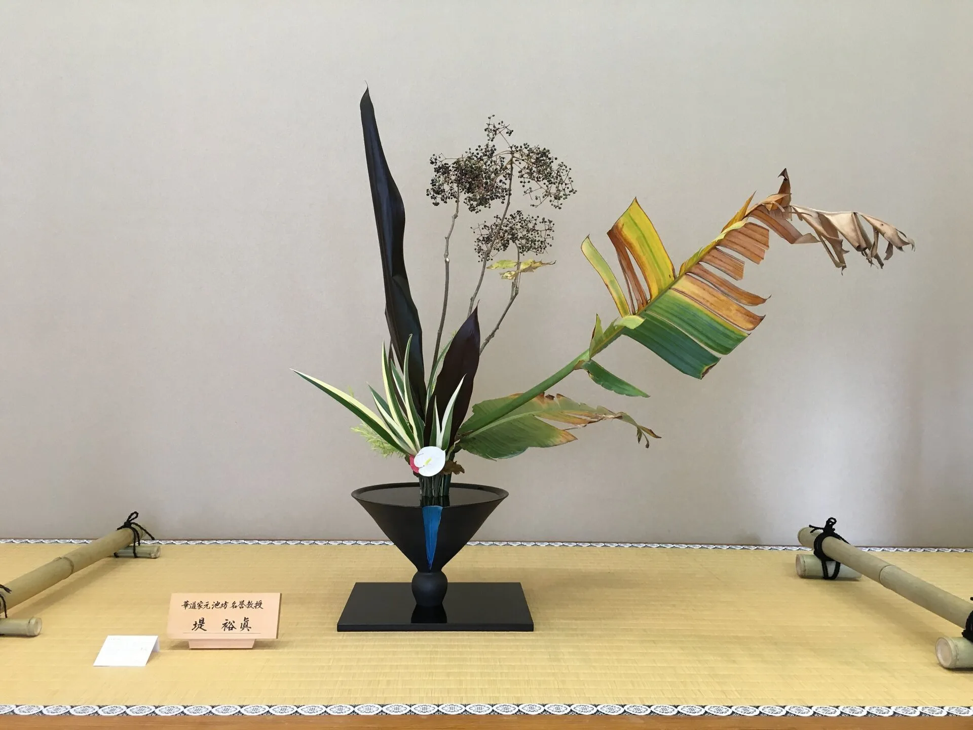 Tall rikka arrangement of branches and leaves in a dark bronze vase