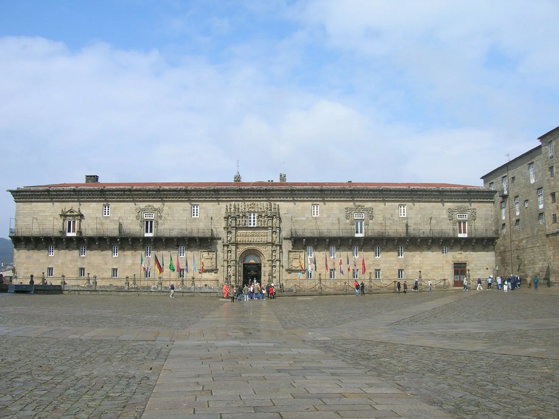 Long stone building with an ornate central doorway facing a paved square