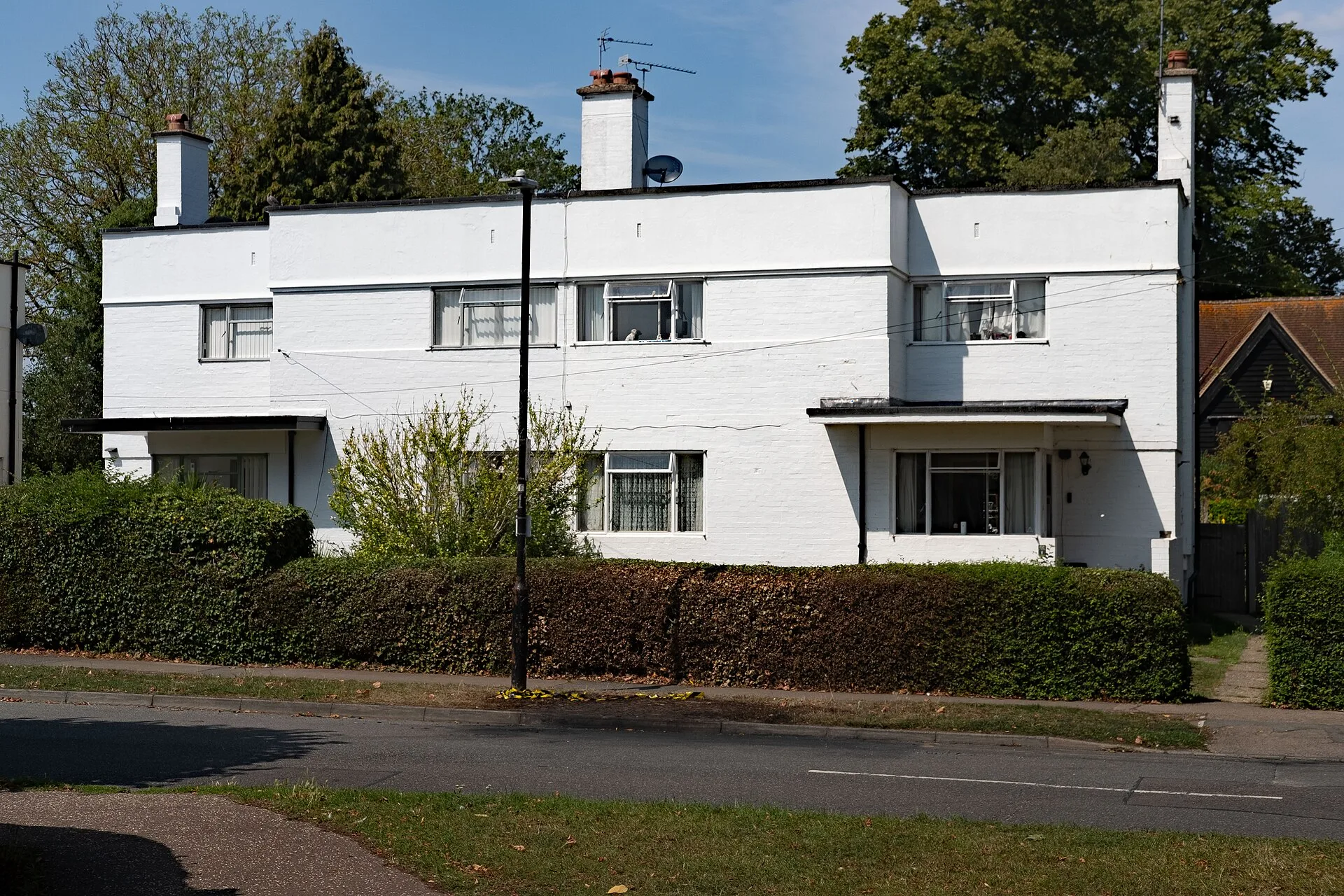 White flat-roofed Modernist house with metal windows behind a hedge and lawn