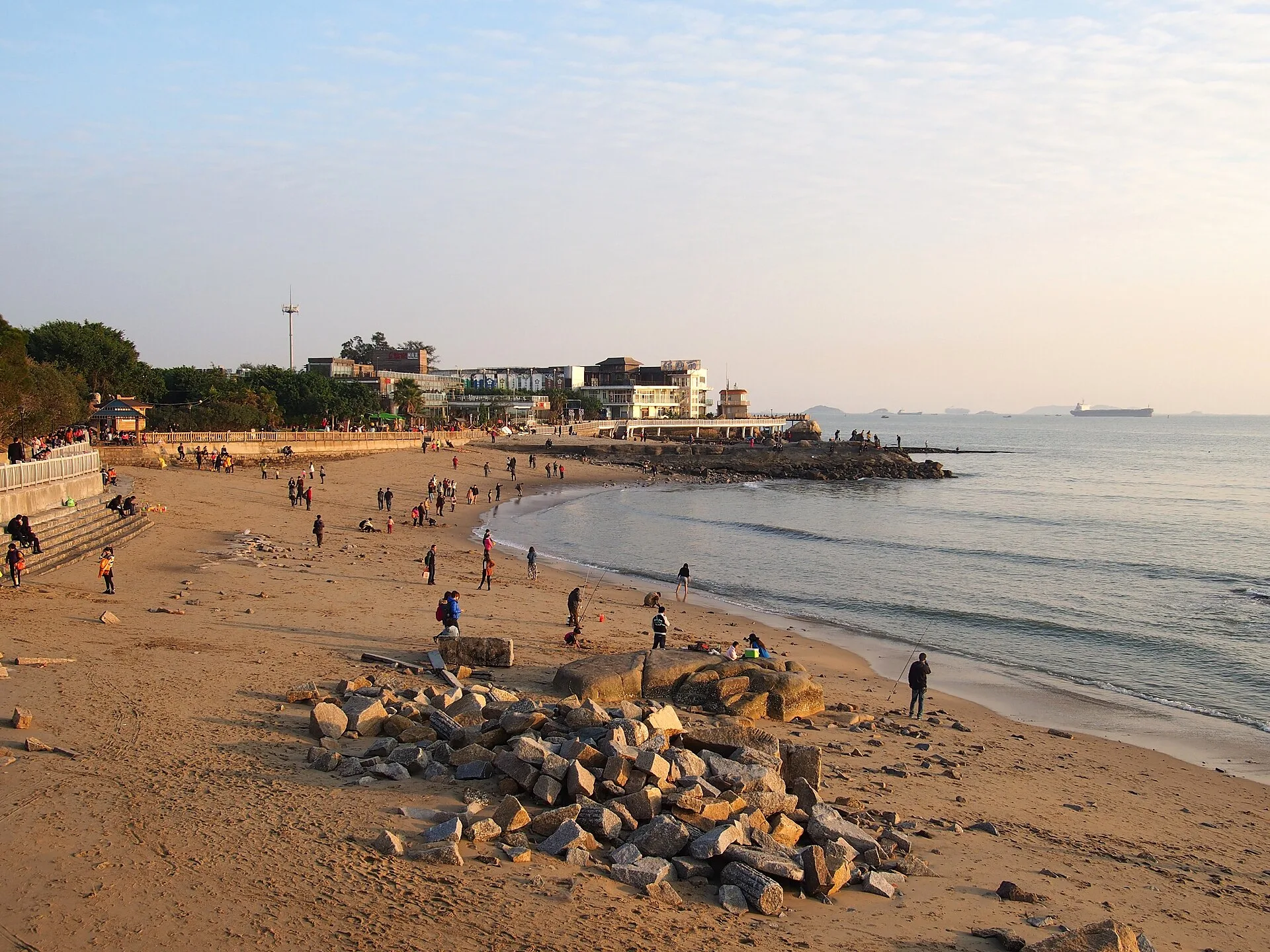 Sandy beach with a pile of rocks, people walking and calm sea