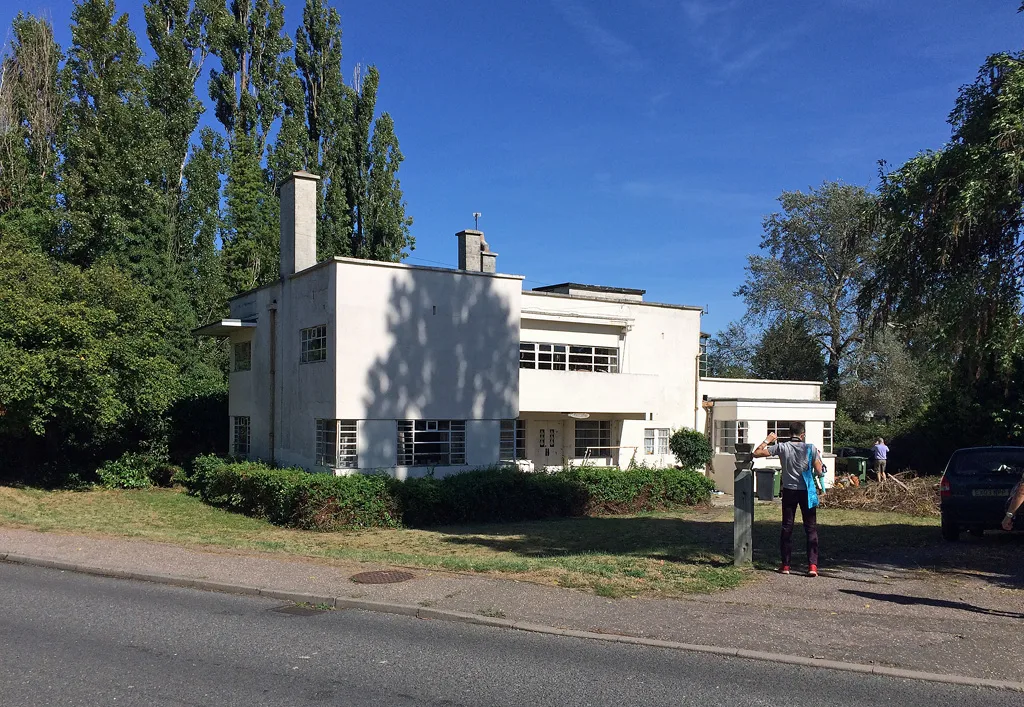 White flat-roofed Modernist house with stepped blocks behind trees and lawn