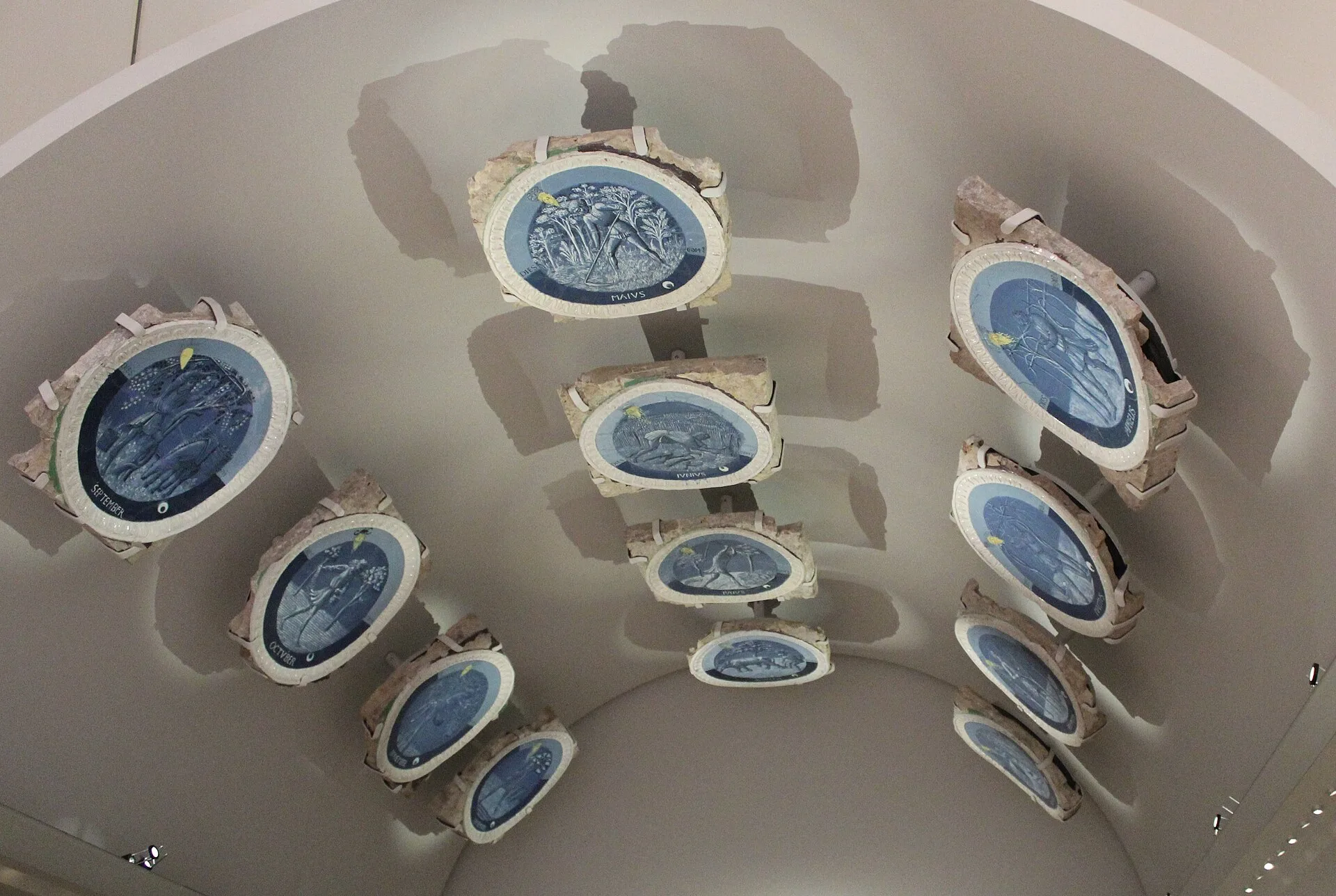 Twelve blue and white glazed roundels displayed on a curved museum ceiling