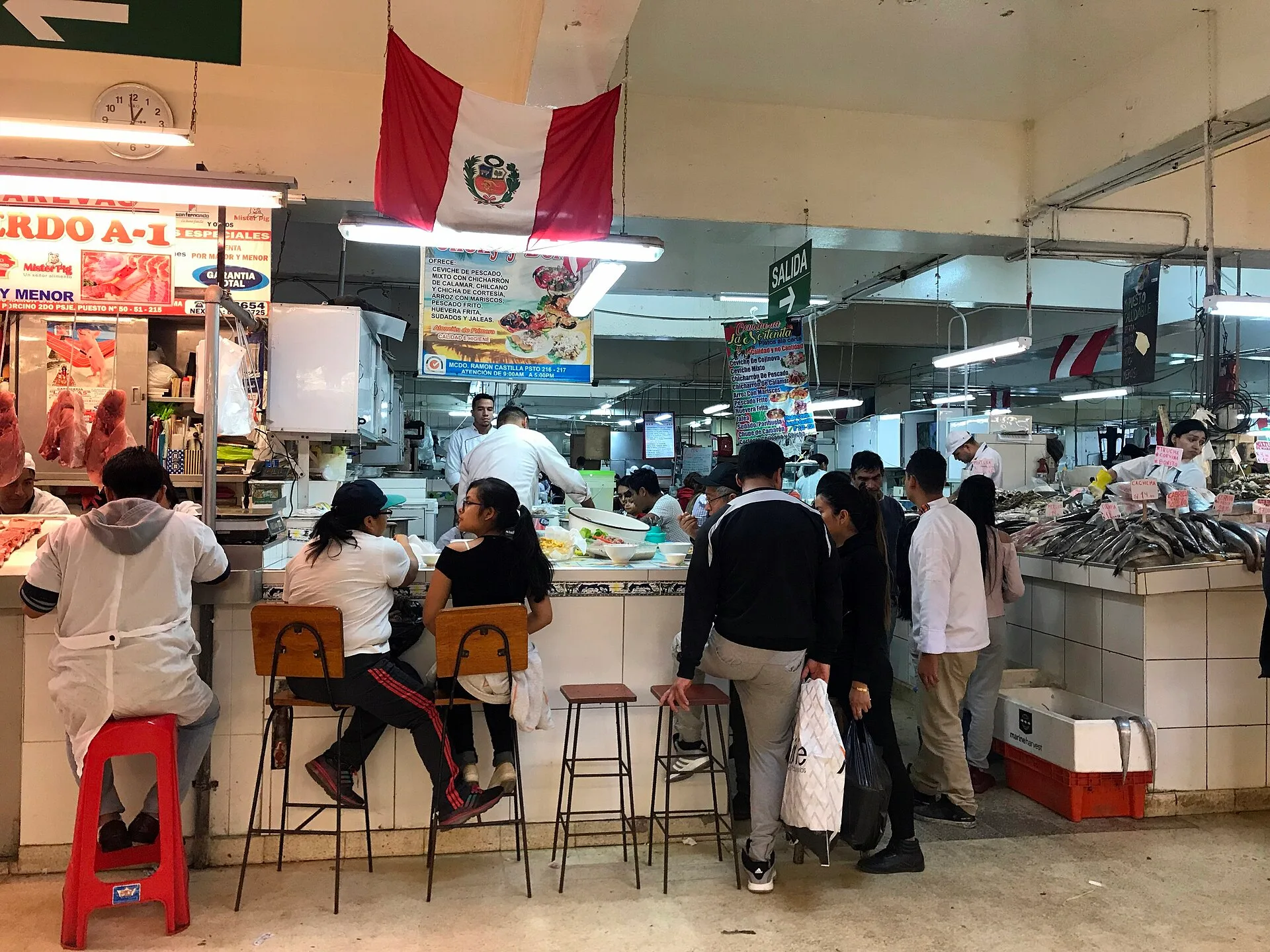 Market food counter with stools, customers and a menu board