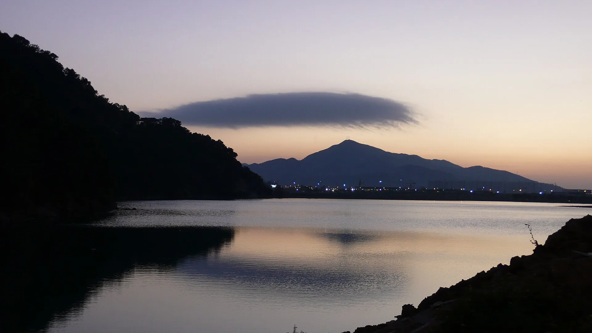 Calm lake at dusk with hills silhouetted against an orange sky