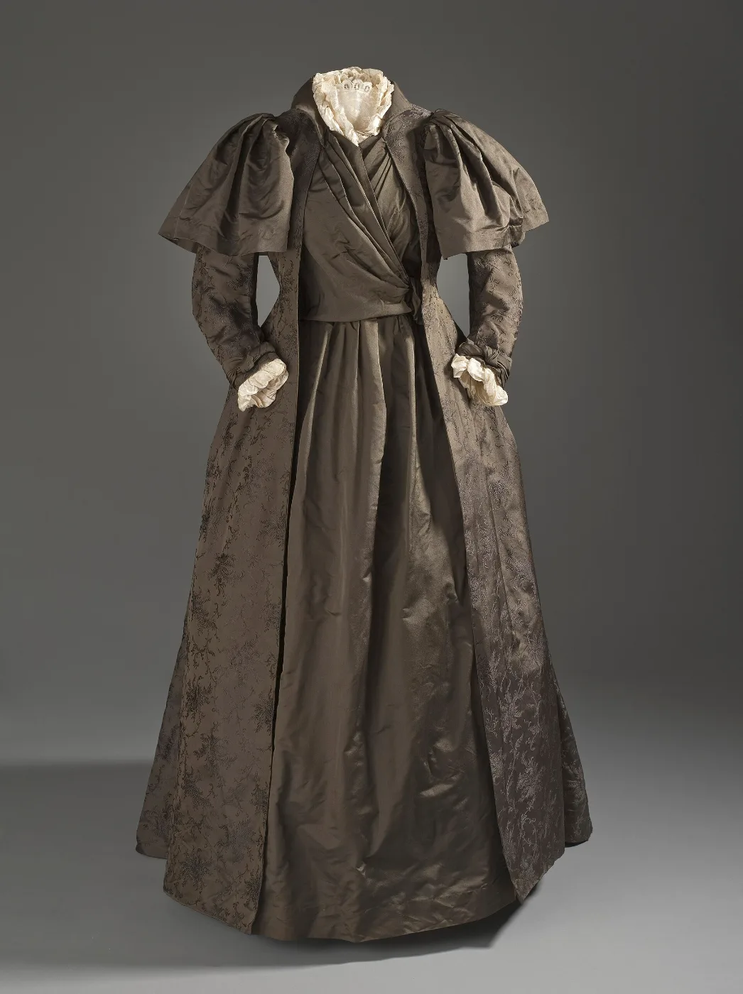 Dark patterned silk tea gown with puffed sleeves displayed on a dress form