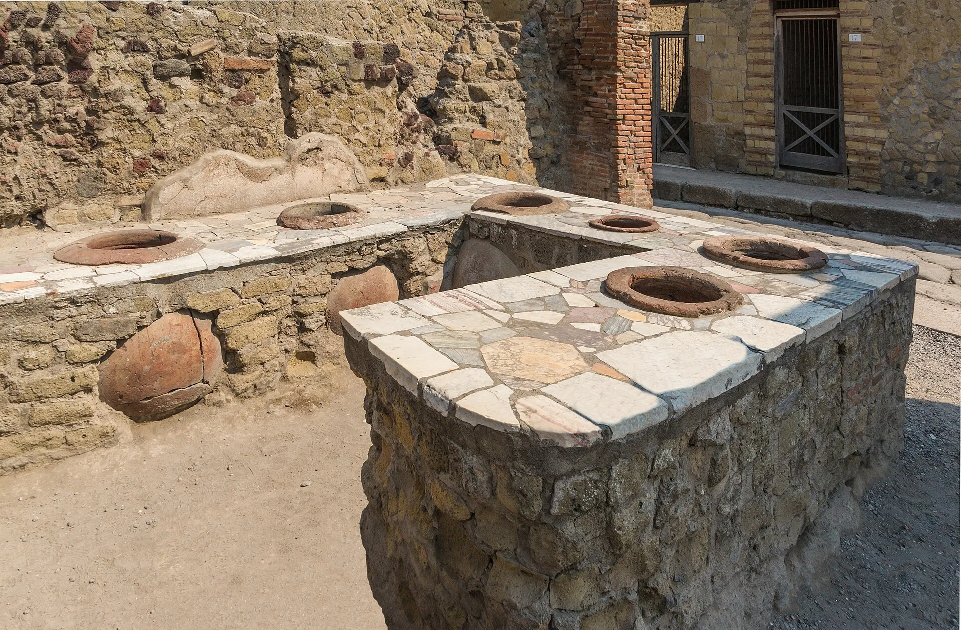 Ruined Roman counter with embedded storage jars inside a stone-walled room
